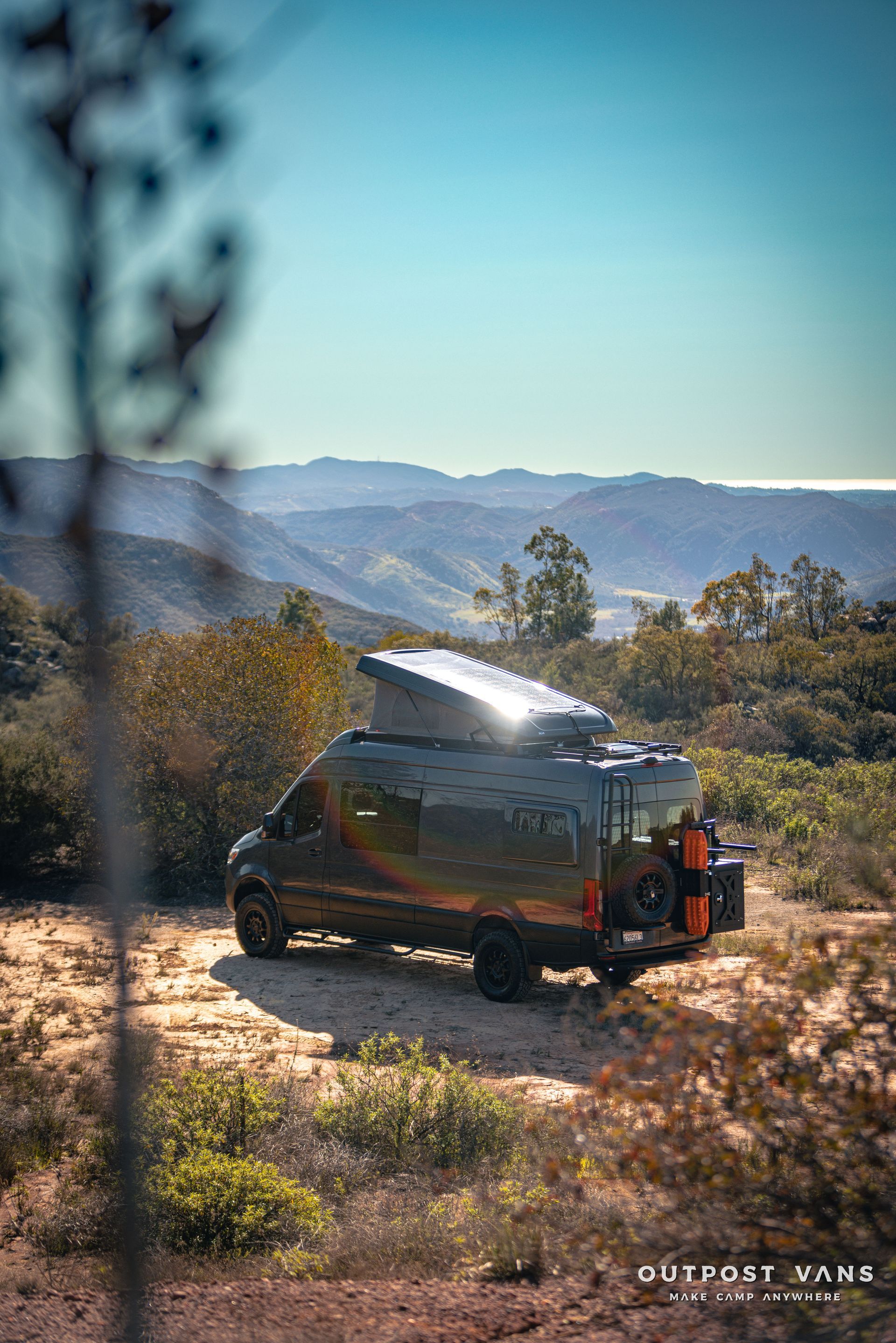a van is parked on top of a dirt hill with mountains in the background .