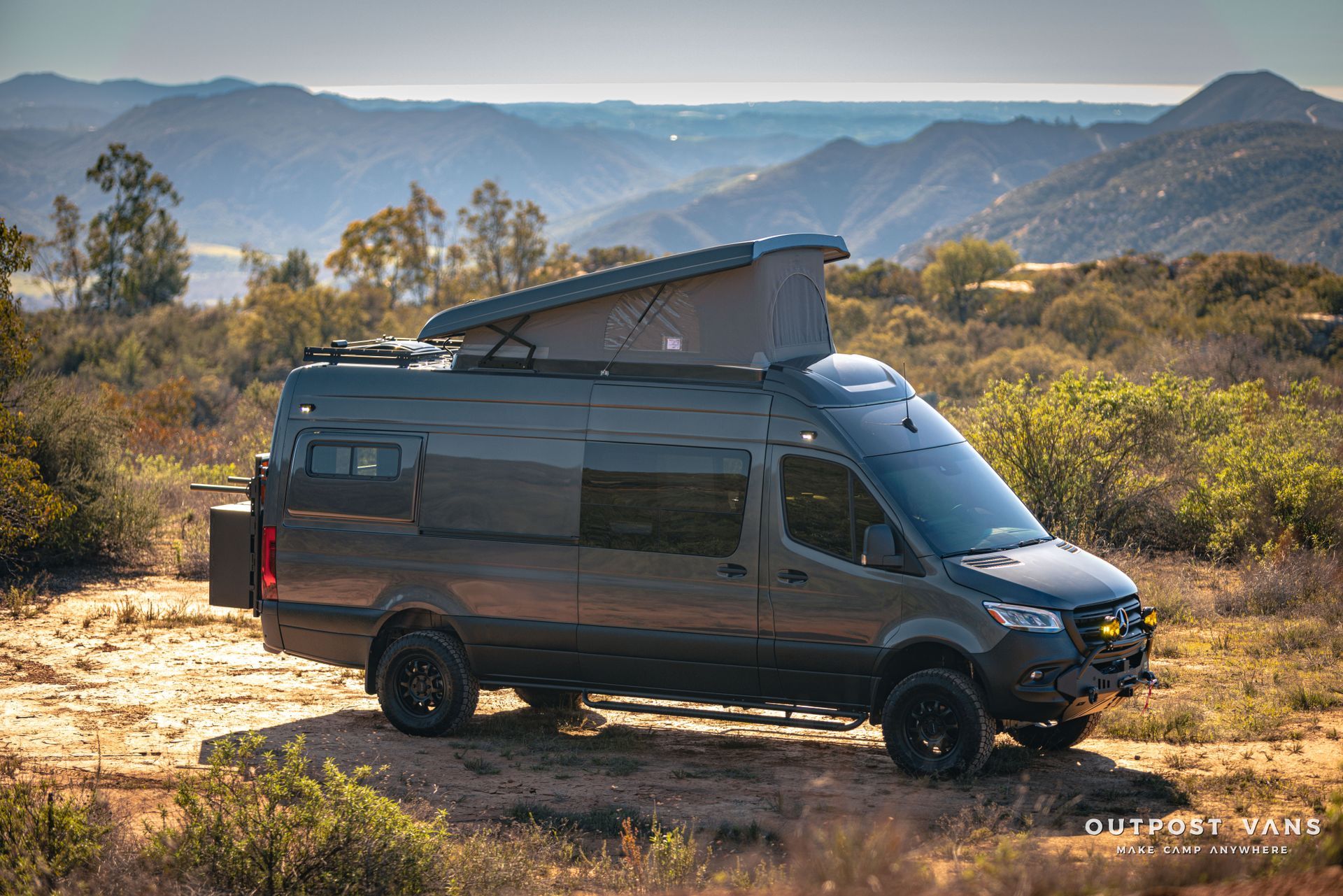 a van with a pop up roof is parked in a field with mountains in the background .