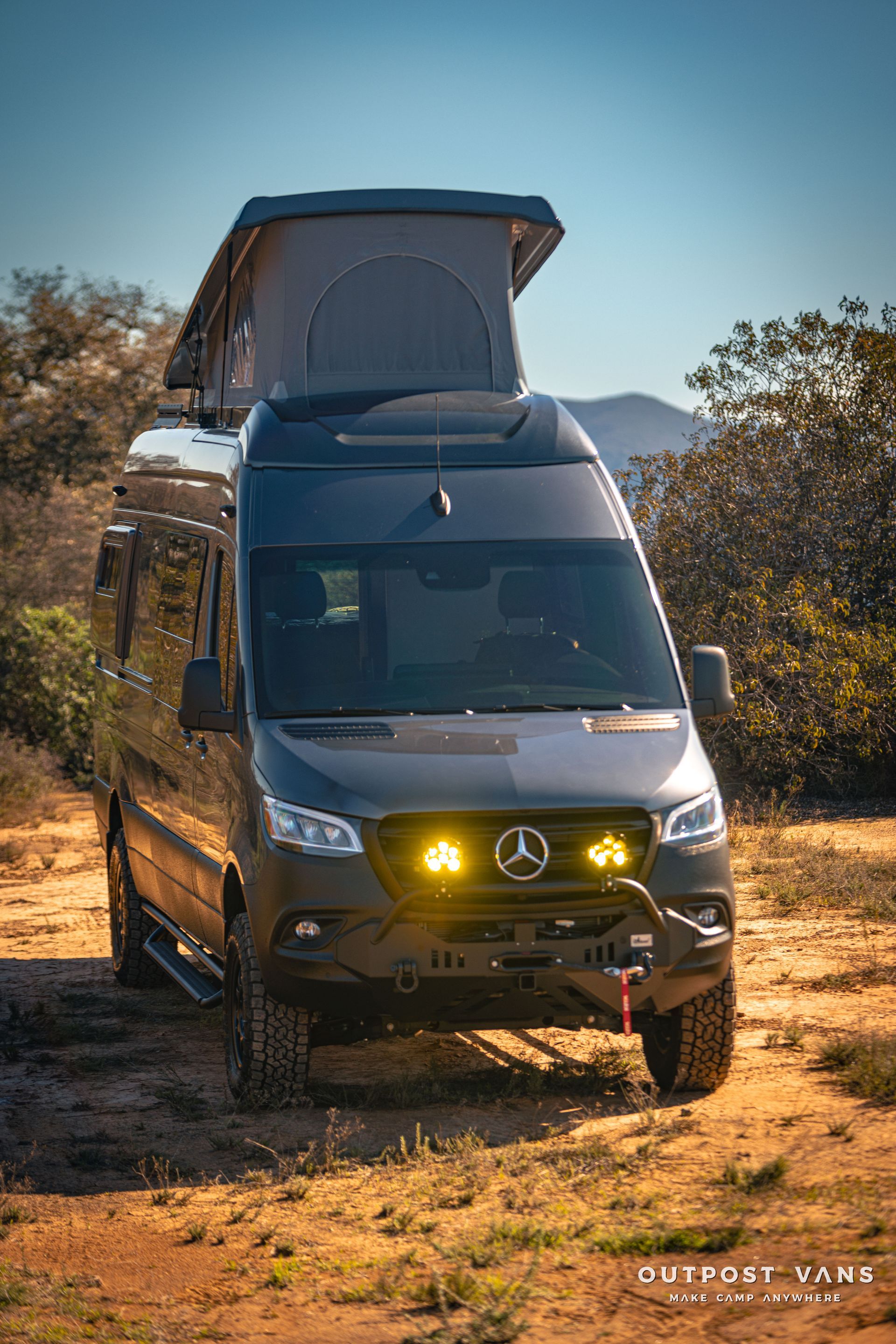 a mercedes sprinter van with a pop up roof is parked in a dirt field .