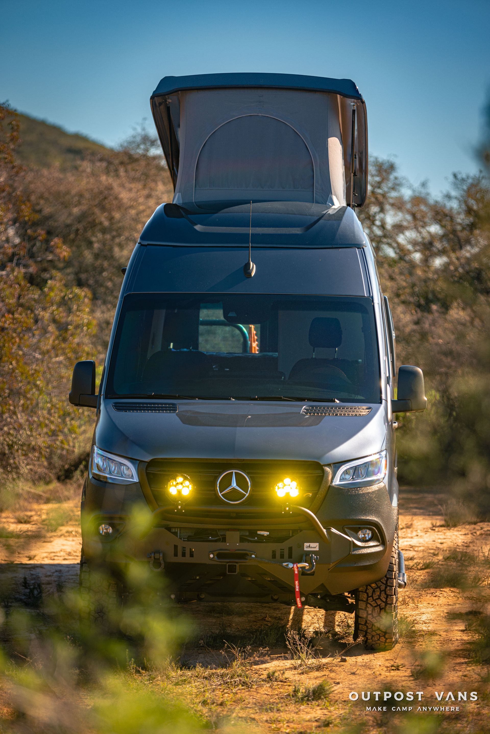 a mercedes sprinter van with a pop up roof is parked on a dirt road .