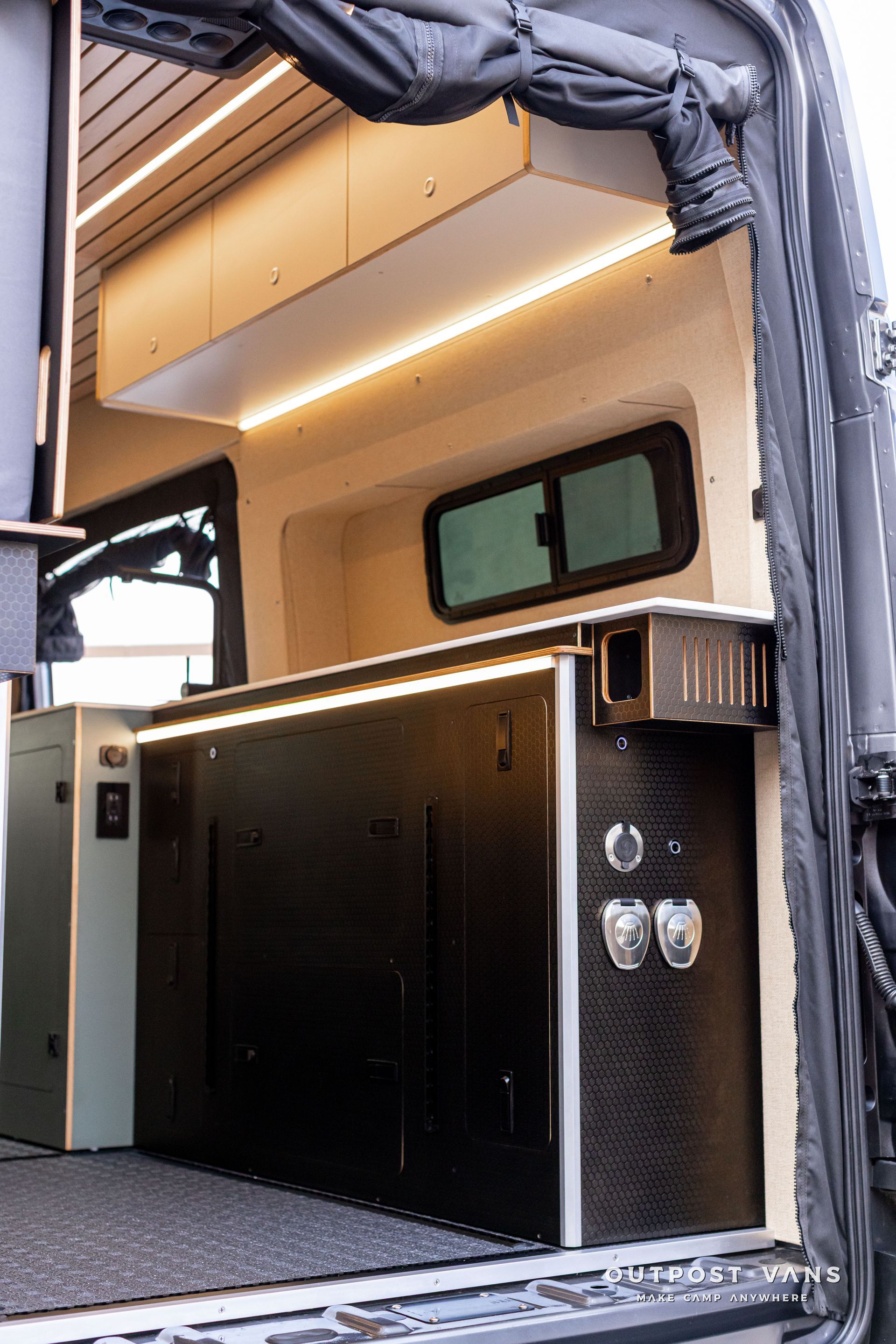 Compact camper van interior with black cabinetry, beige ceiling, and small window under an awning