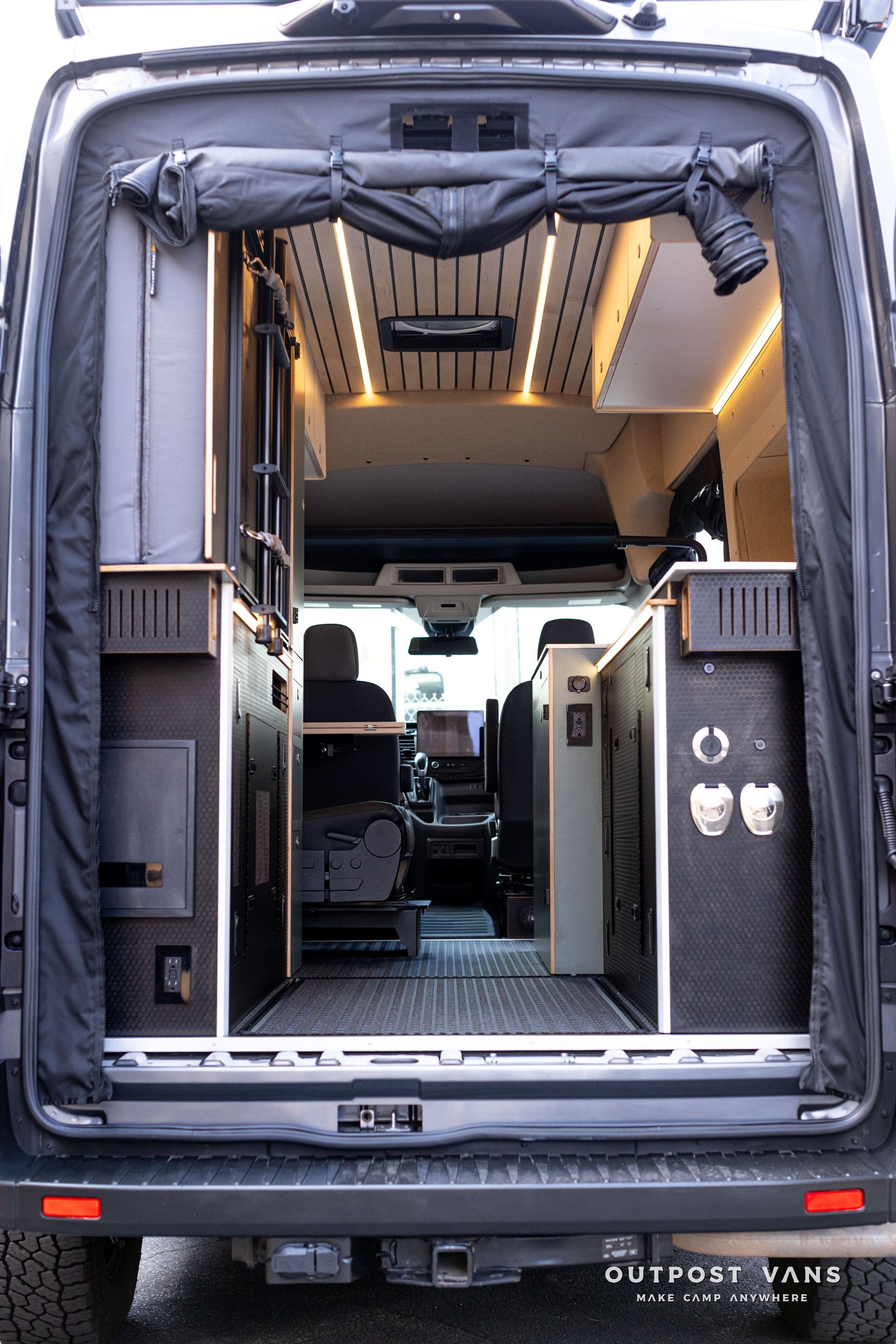 Open rear van doorway showing a customized camper interior with lights, seating, and a center aisle