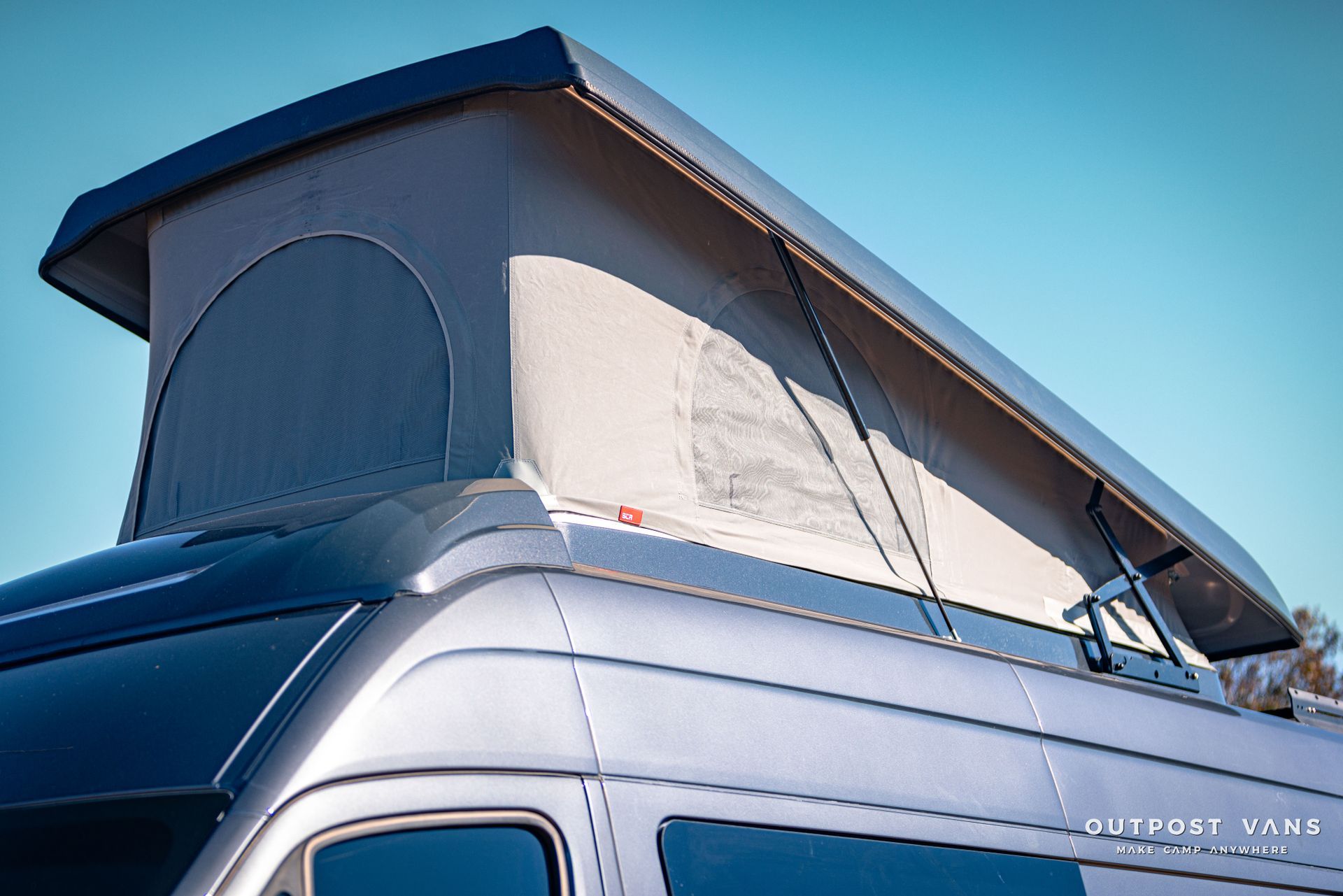 a van with a pop up roof is parked in front of a blue sky .