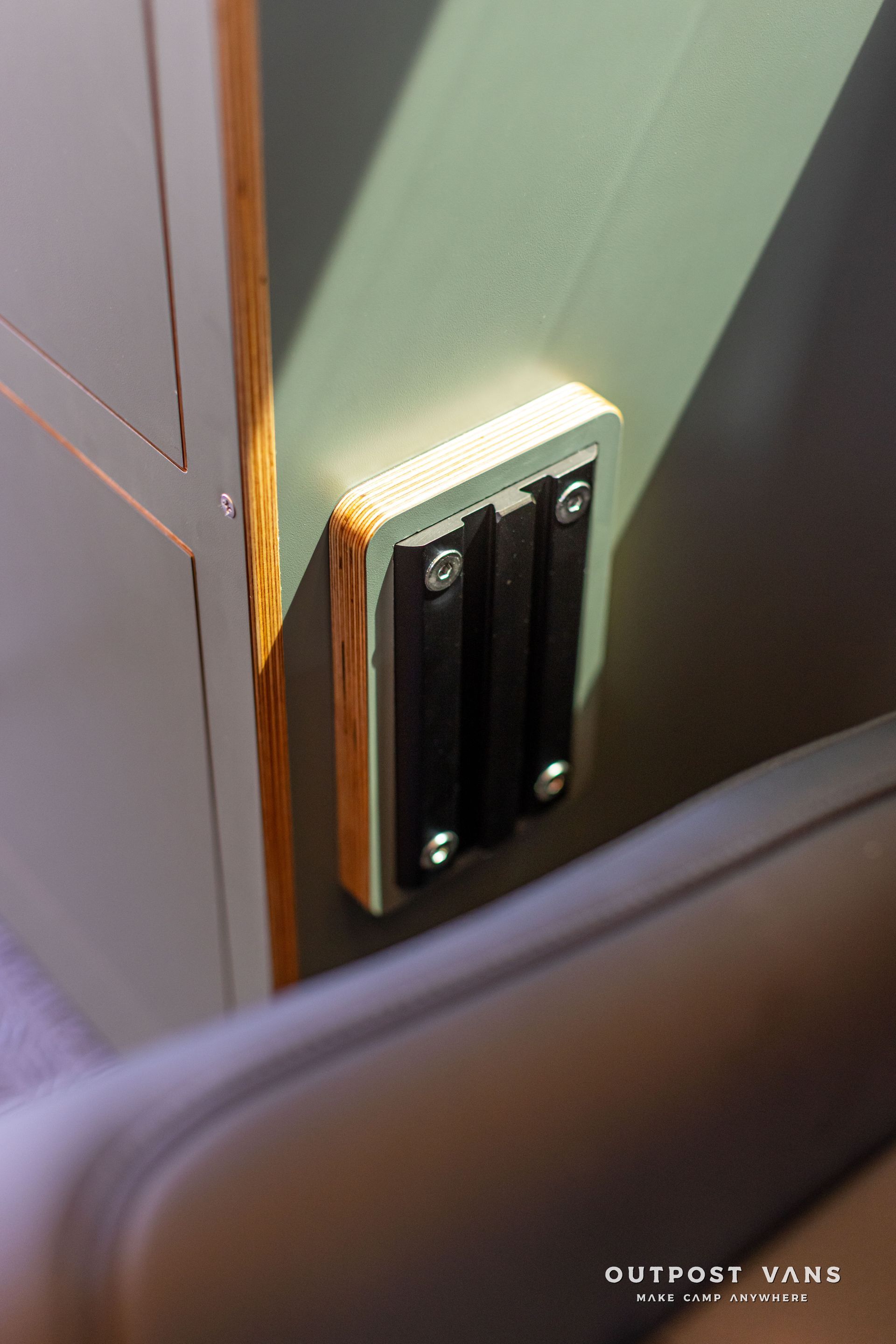 Close-up of a black door latch on a green doorframe with rust around the hinge area.