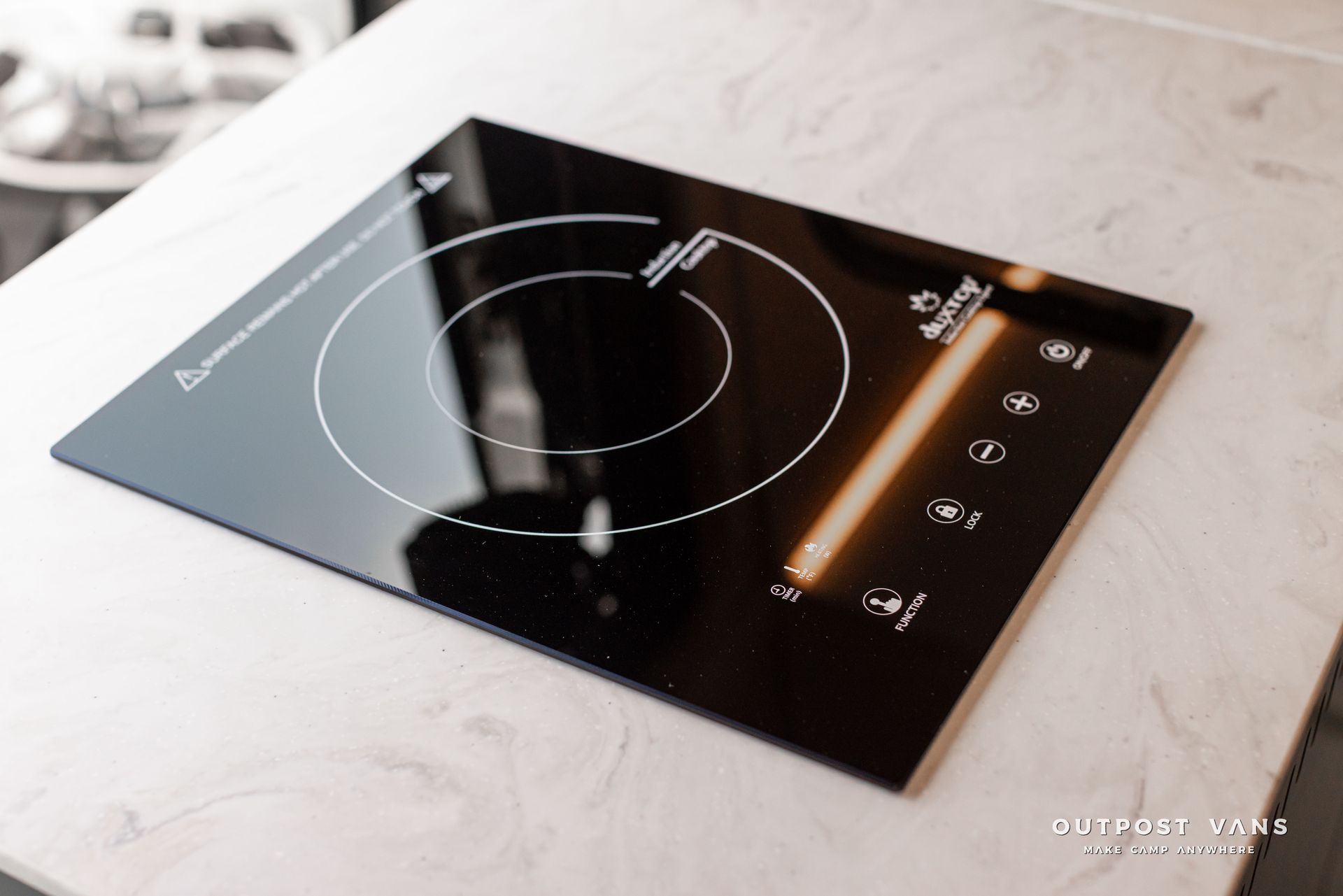 Black glass induction cooktop with touch controls on a light marble countertop