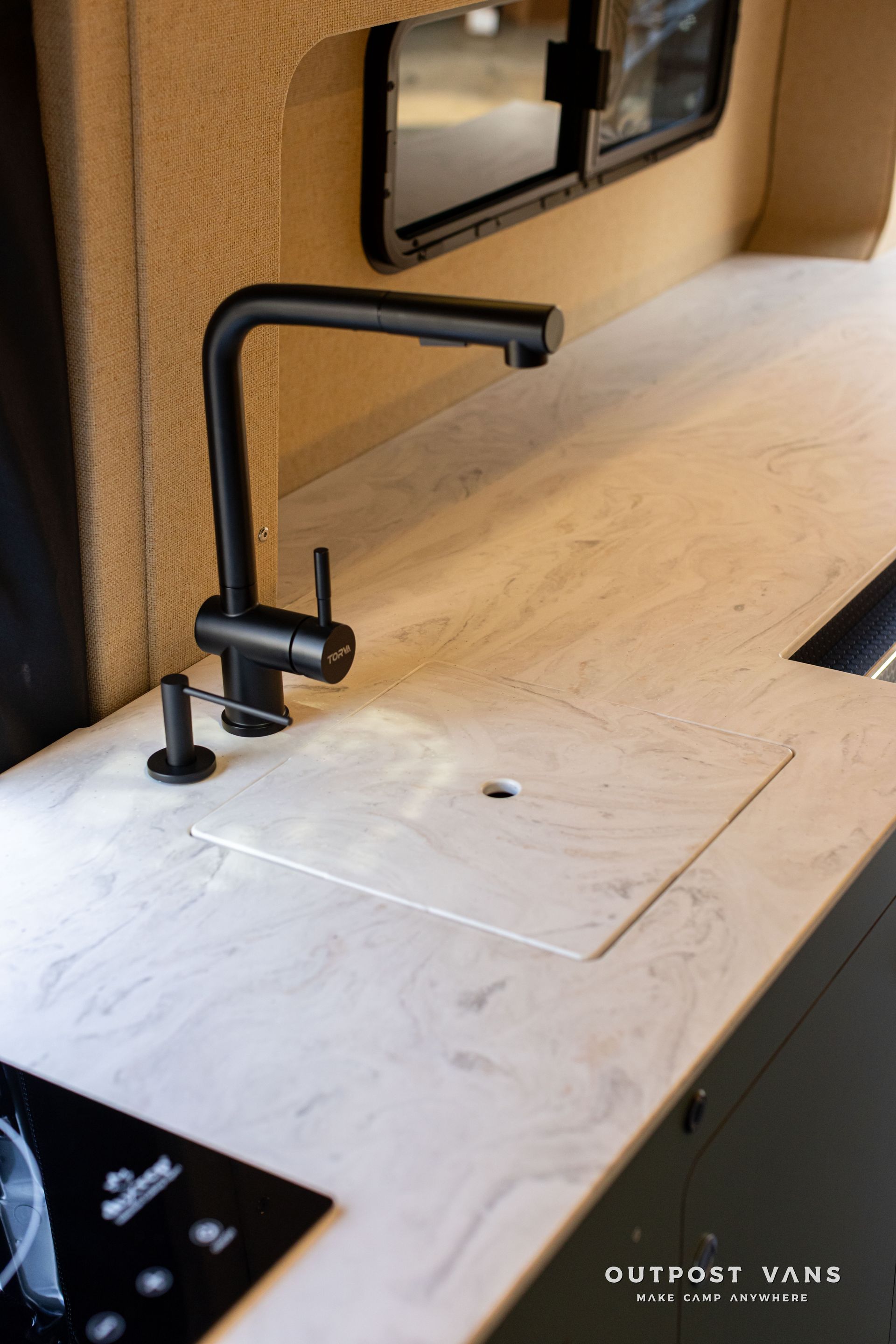 Compact wood-toned camper sink with matte black faucet and countertop in a small kitchen area