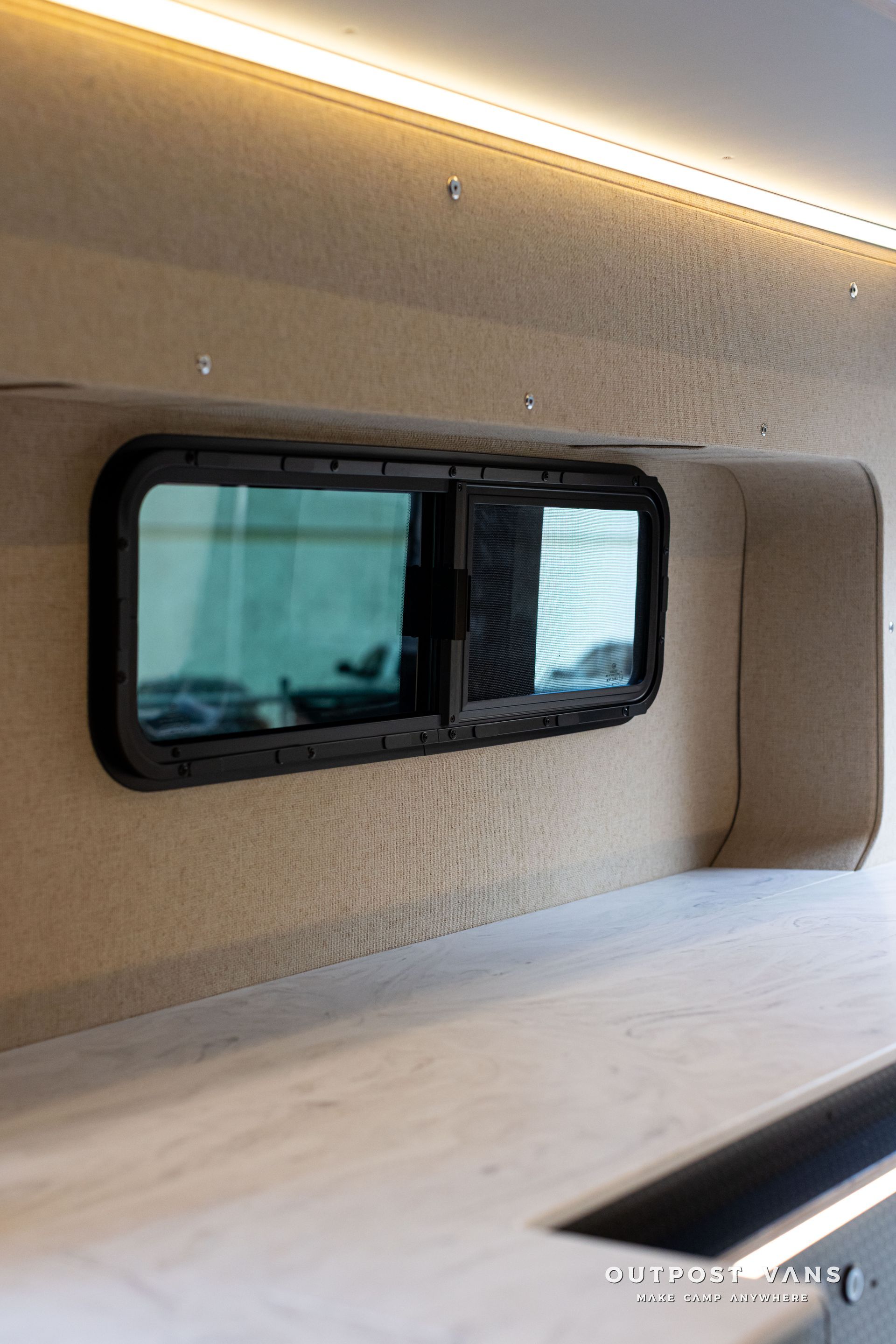 Interior of a modern RV or camper with a tinted window, beige walls, and LED ceiling lighting