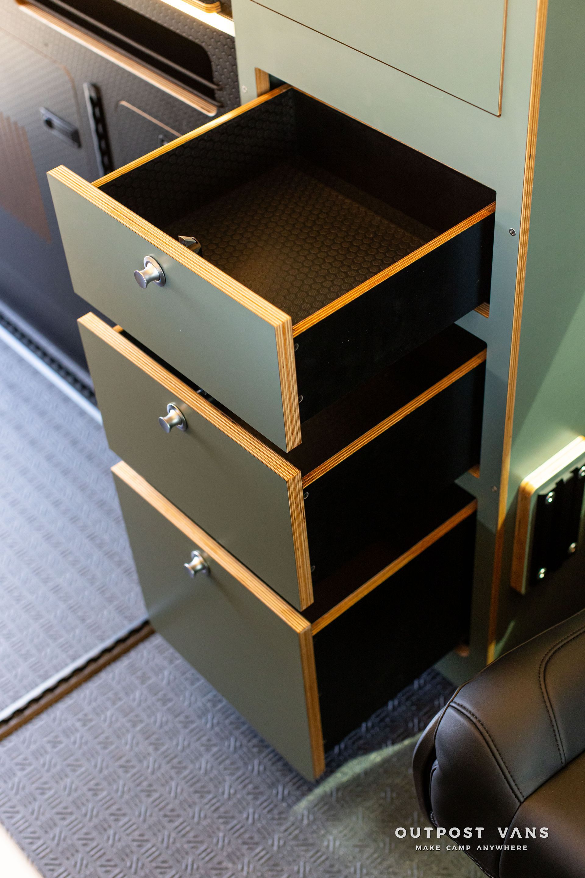 Open drawer cabinet in a vehicle aisle, showing dark interior and three gray drawers with wooden edges.
