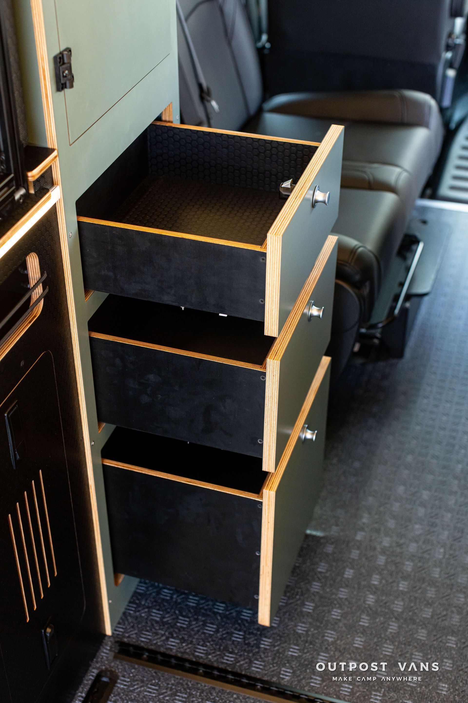 Stacked black storage drawers beside a vehicle seat inside a transport compartment