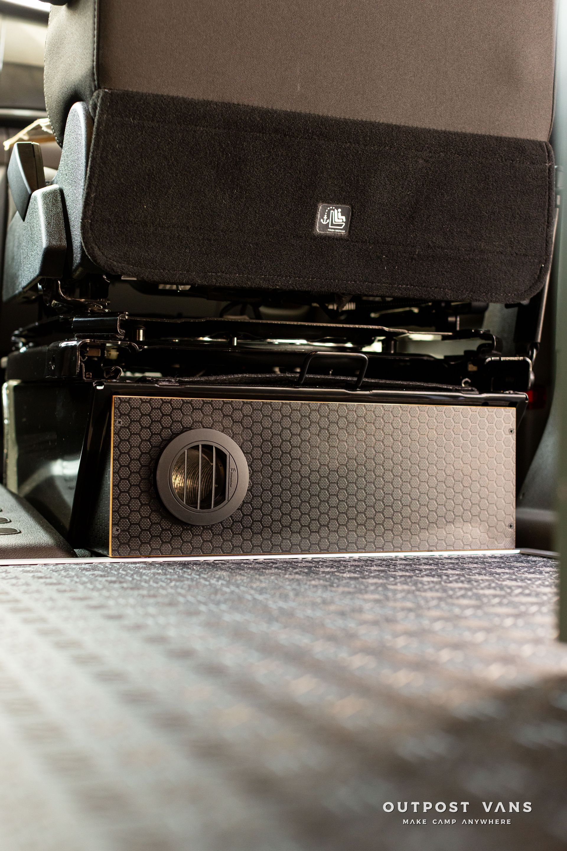 Close-up of a black and silver seat base with a round control knob and textured carpeted floor.