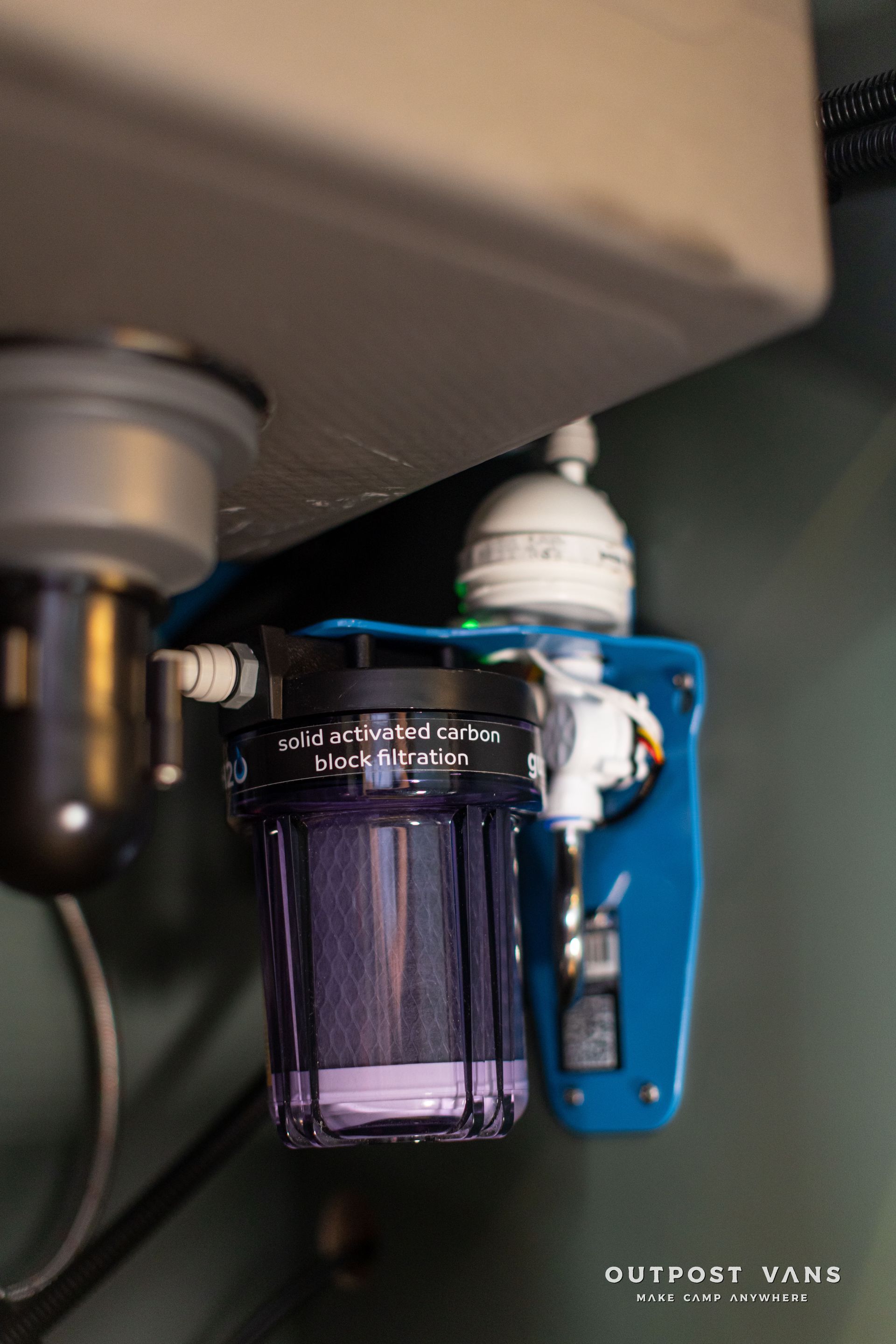 Under-sink water filter and fittings mounted on a blue bracket under a countertop