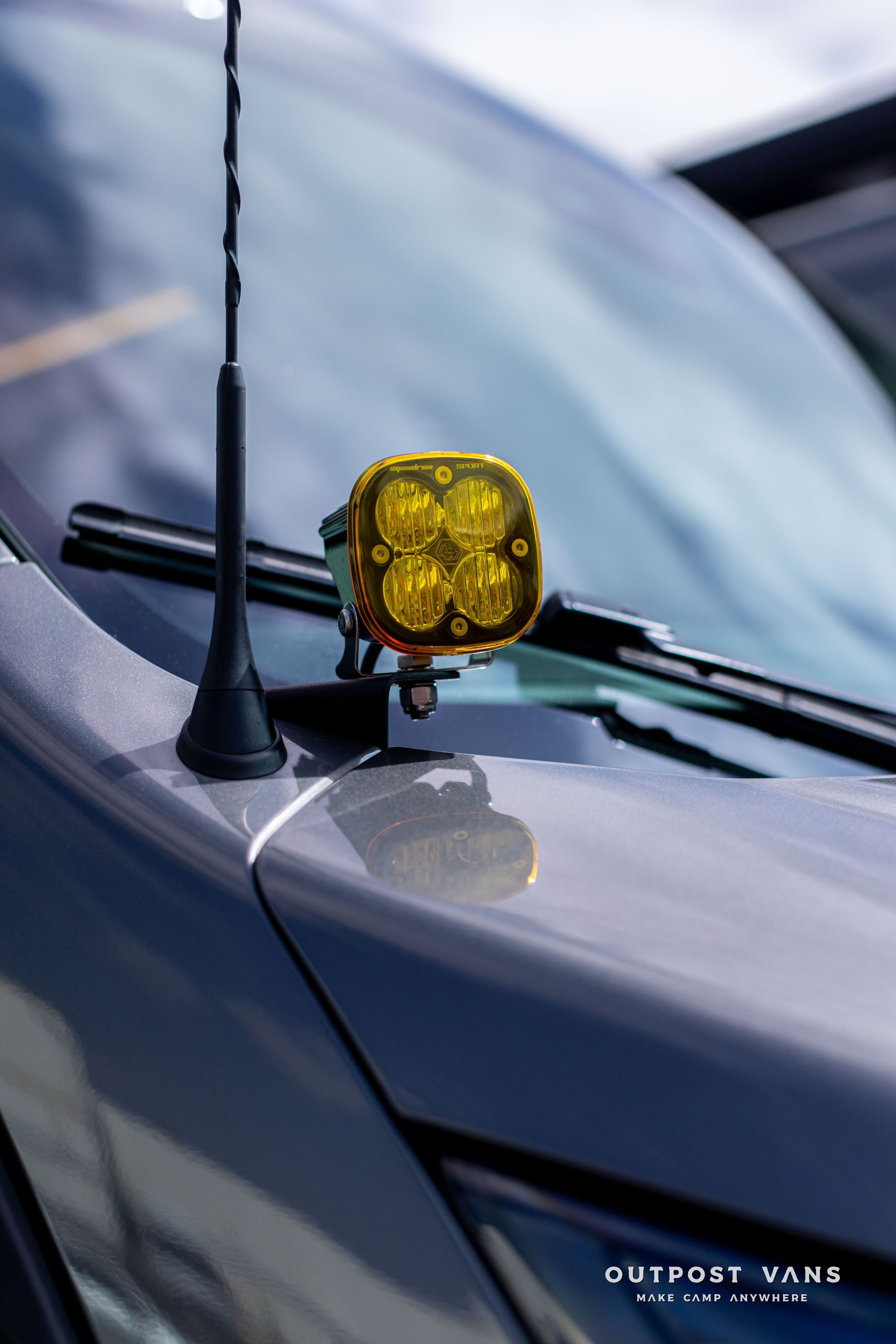 Yellow light mounted on a car hood near the windshield, with a black antenna visible.