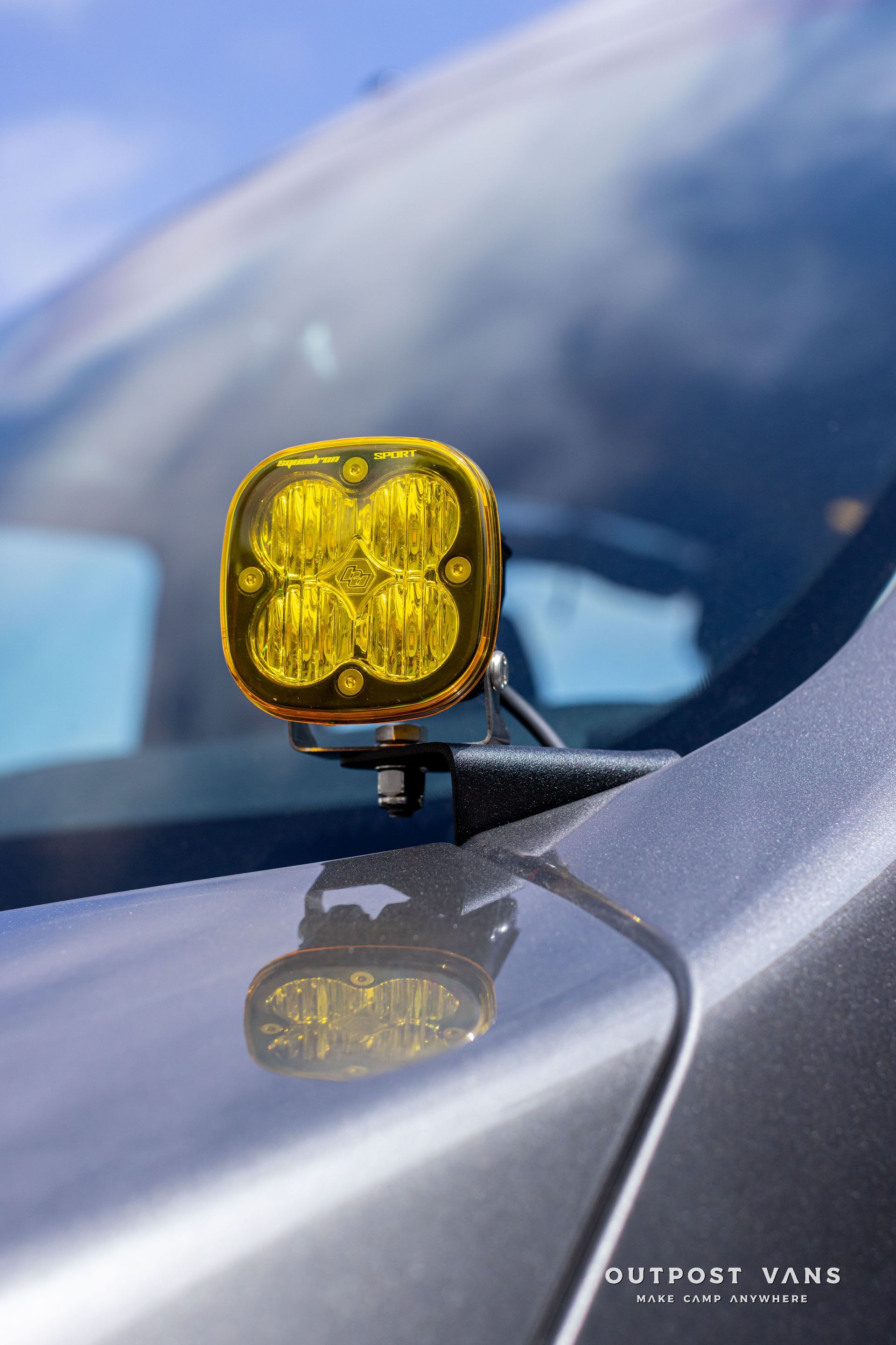 Yellow off-road light mounted on a car hood, with the windshield blurred in the background