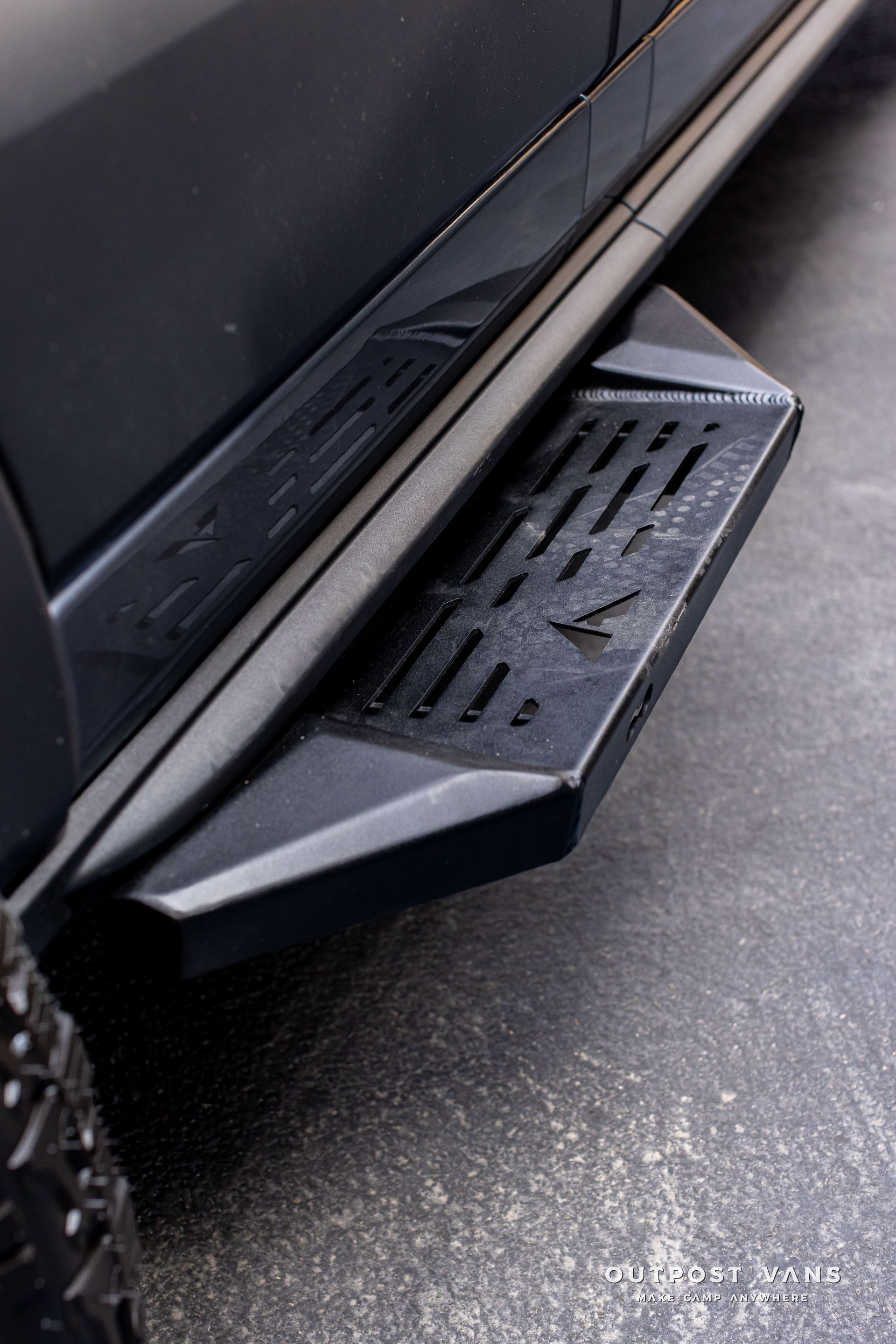 Black vehicle side step/running board with textured tread and angled support on pavement