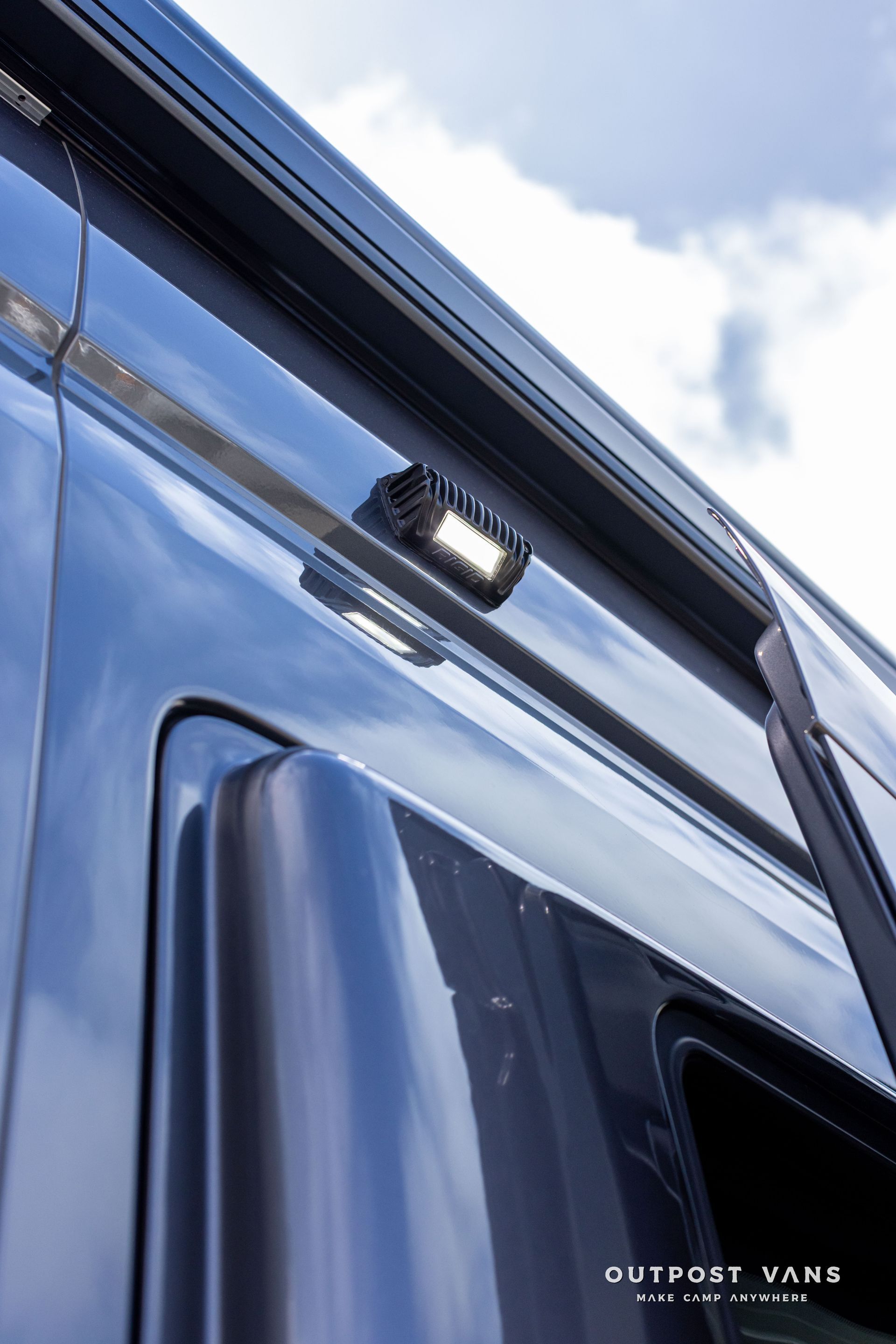 Close-up of a blue van’s side mirror and roof edge against a cloudy sky