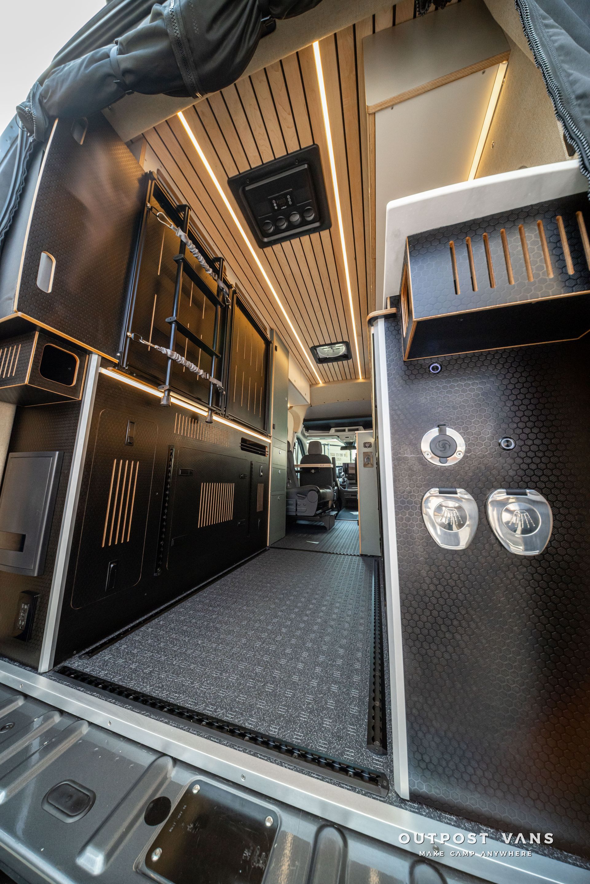 Inside a black camper van interior with cabinets, overhead lights, and a narrow aisle