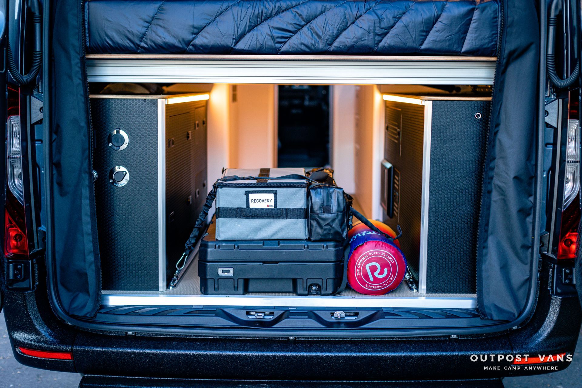 the back of a van with a bed and luggage in it .