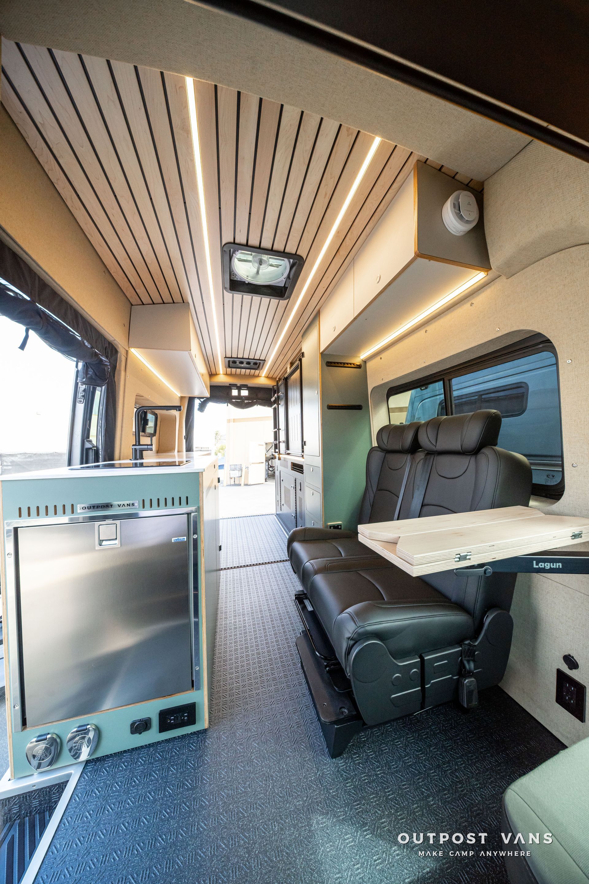 Interior of a camper van with a bench seat, table, cabinets, and skylight ceiling.