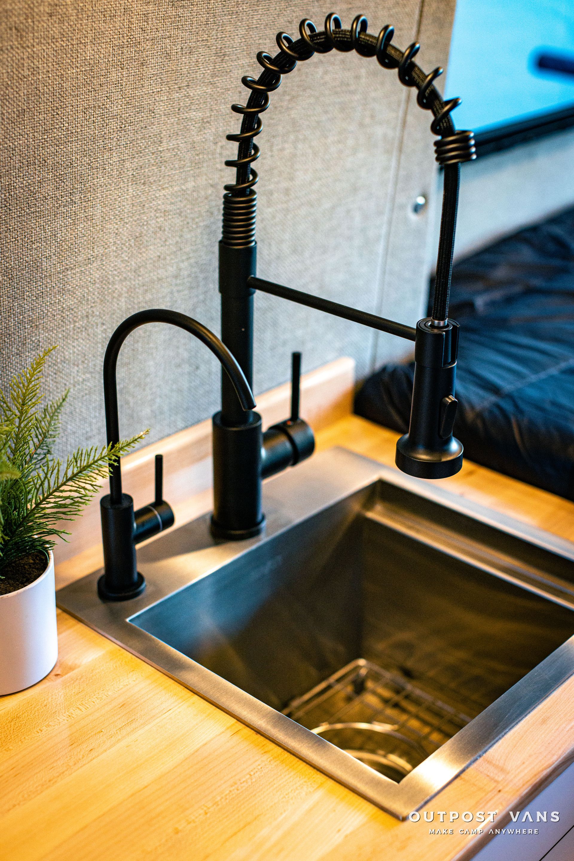 a kitchen sink with a black faucet and a potted plant .