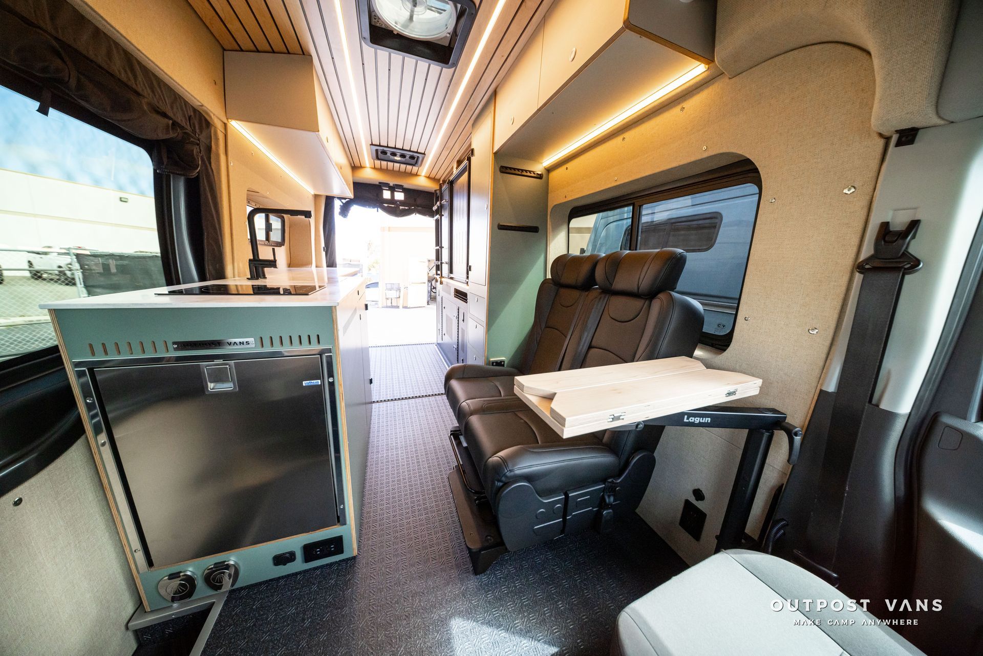 Interior of a luxury van with leather seats, table, and kitchenette, viewed down the aisle toward the front.