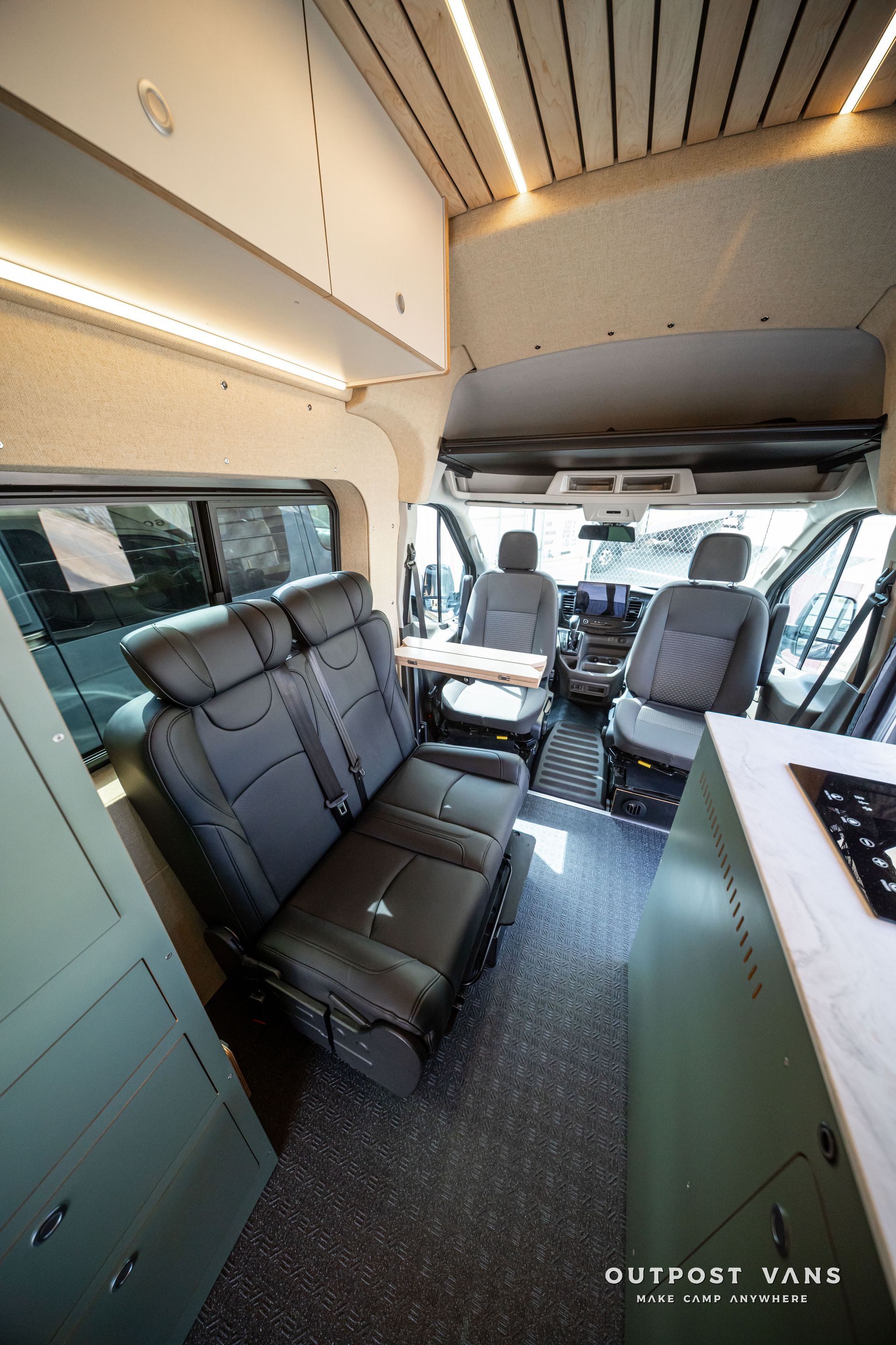 Compact camper van interior with two dark bench seats, overhead storage, and a front cab view