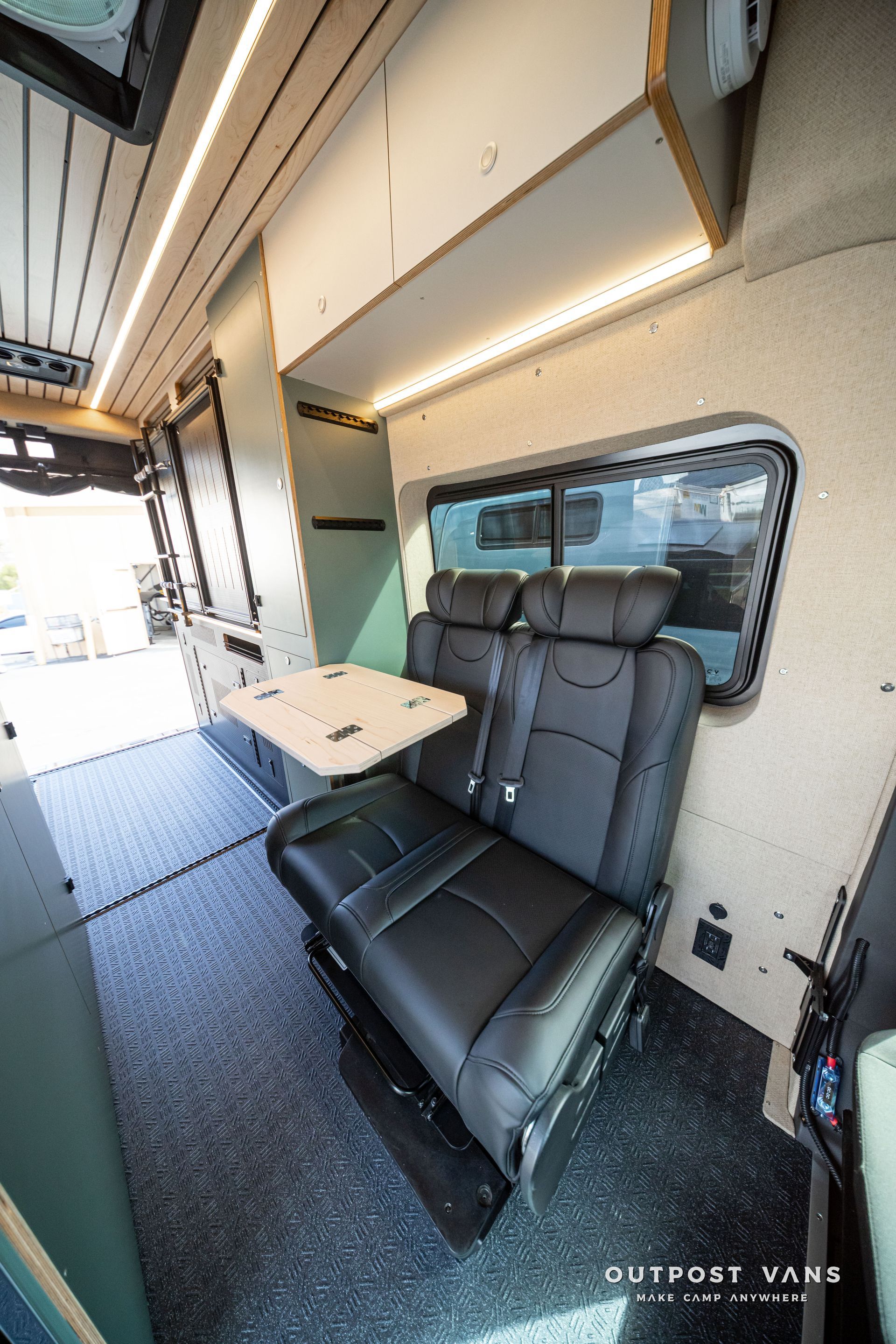 Interior of a camper van with a black bench seat, small table, and side window.