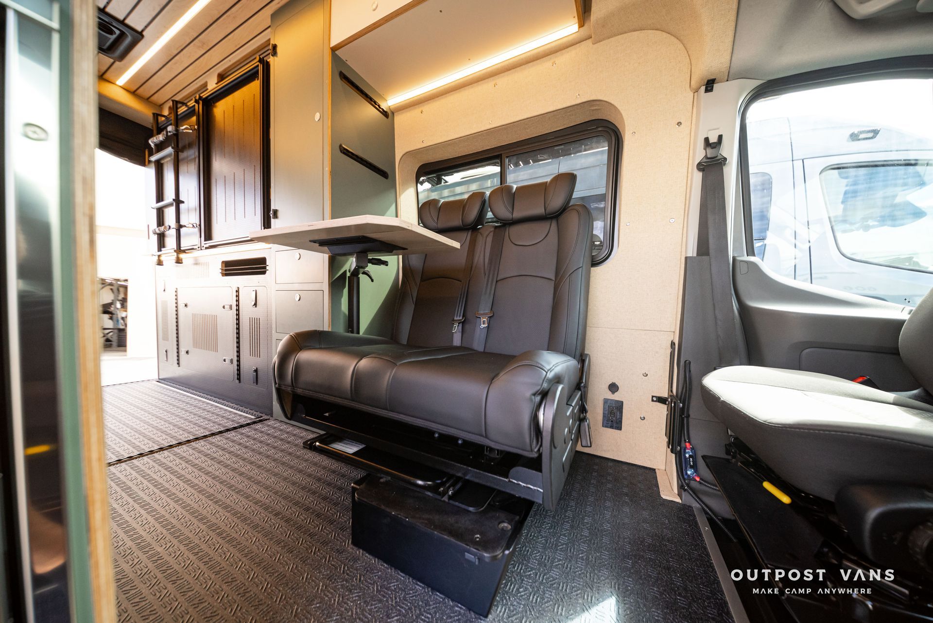Compact RV interior with black bench seat, cabinetry, and warm lighting.