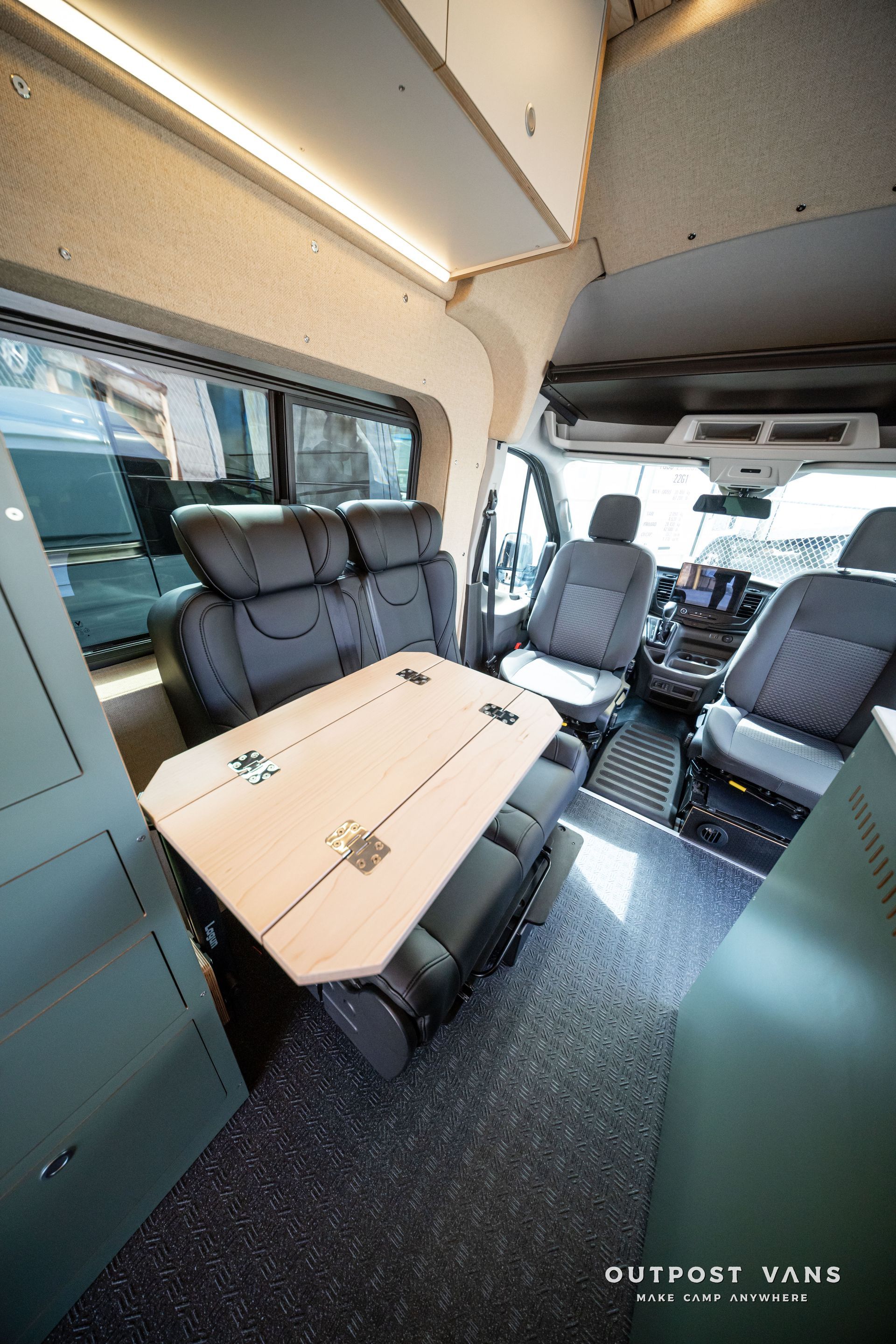 Compact camper van interior with bench seats, fold-out table, and overhead storage cabinets