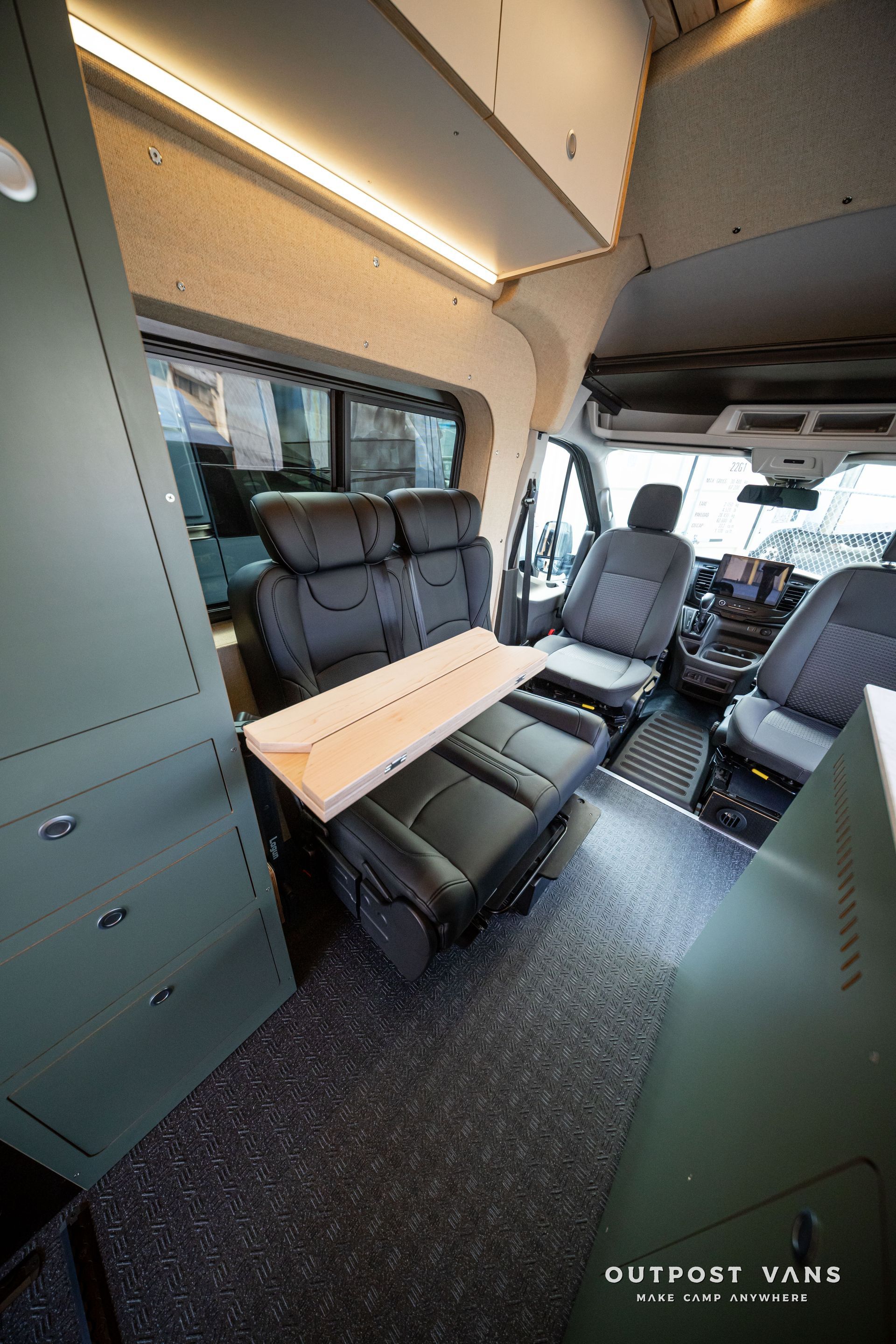 Camper van interior with two seats, a fold-out table, cabinets, and overhead lighting