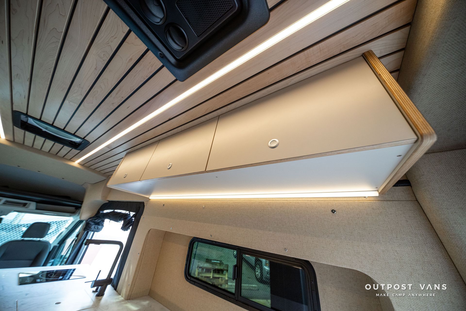 Interior of a modern vehicle with a beige overhead storage cabinet and LED lighting, viewed from below