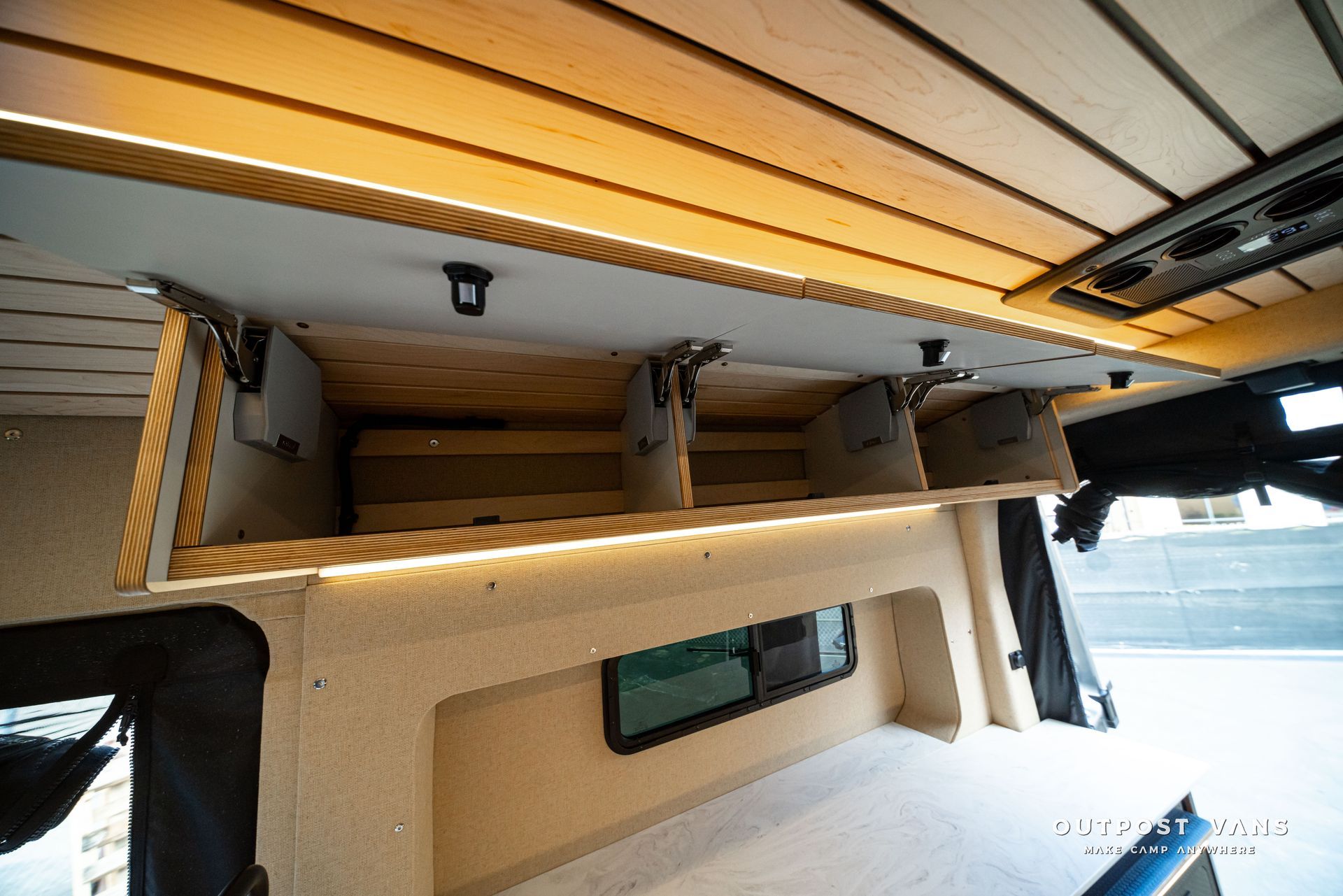 Folded awning and support arms on a beige camper, with ocean visible in the background.