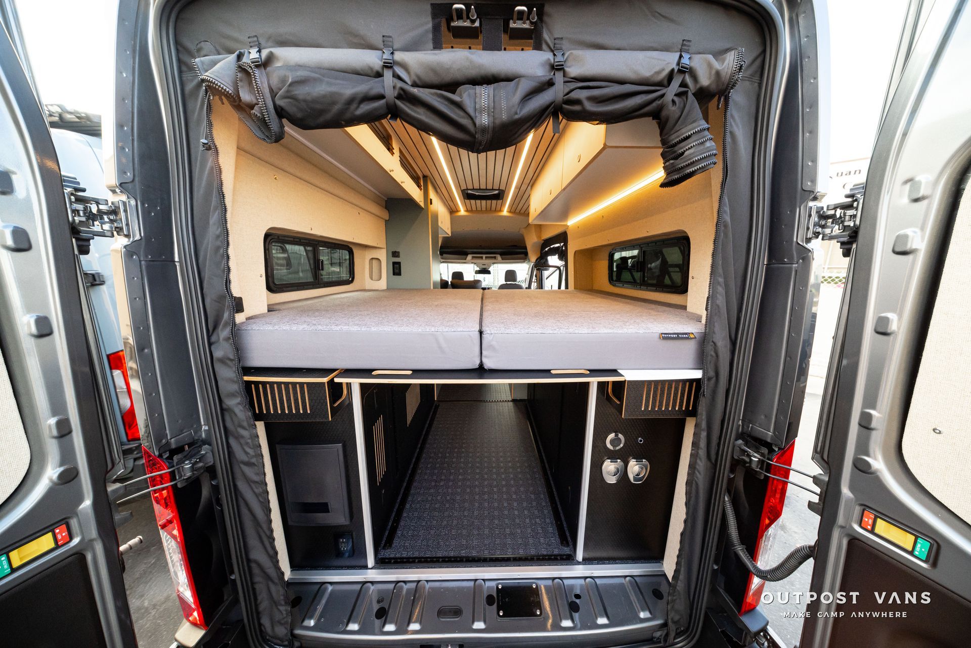 Inside van camper conversion with raised bed, wood cabinetry, and storage area in rear cargo space