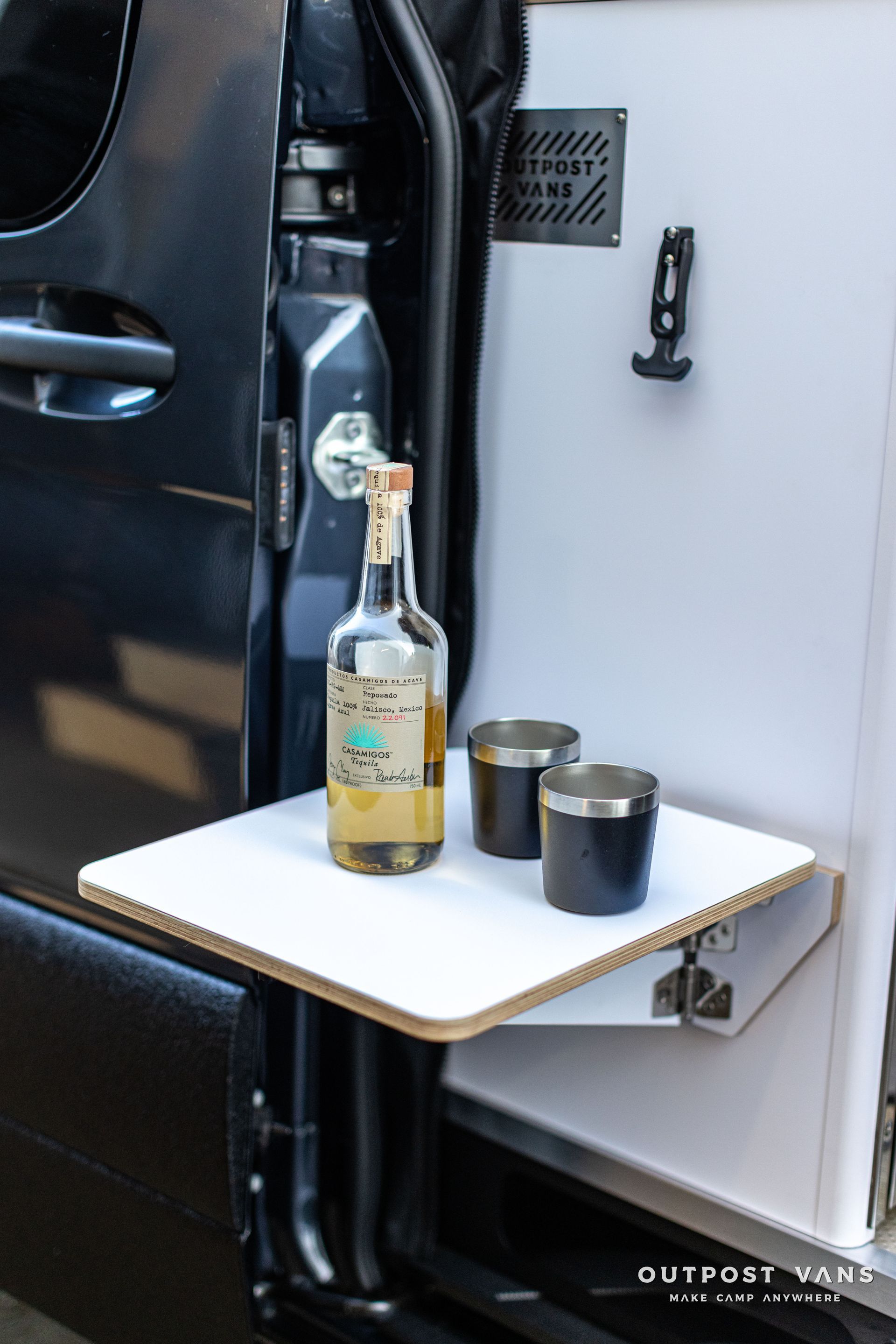 a bottle of tequila and two shot glasses are on a shelf in the back of a van .