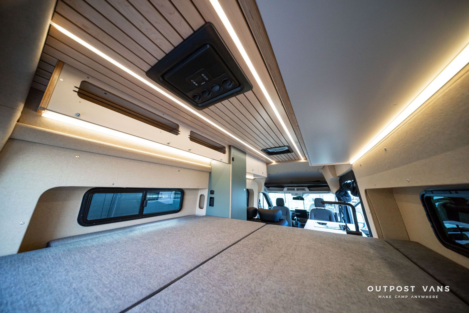 Interior of a camper van with a bed platform, skylight, windows, and warm LED ceiling lights.