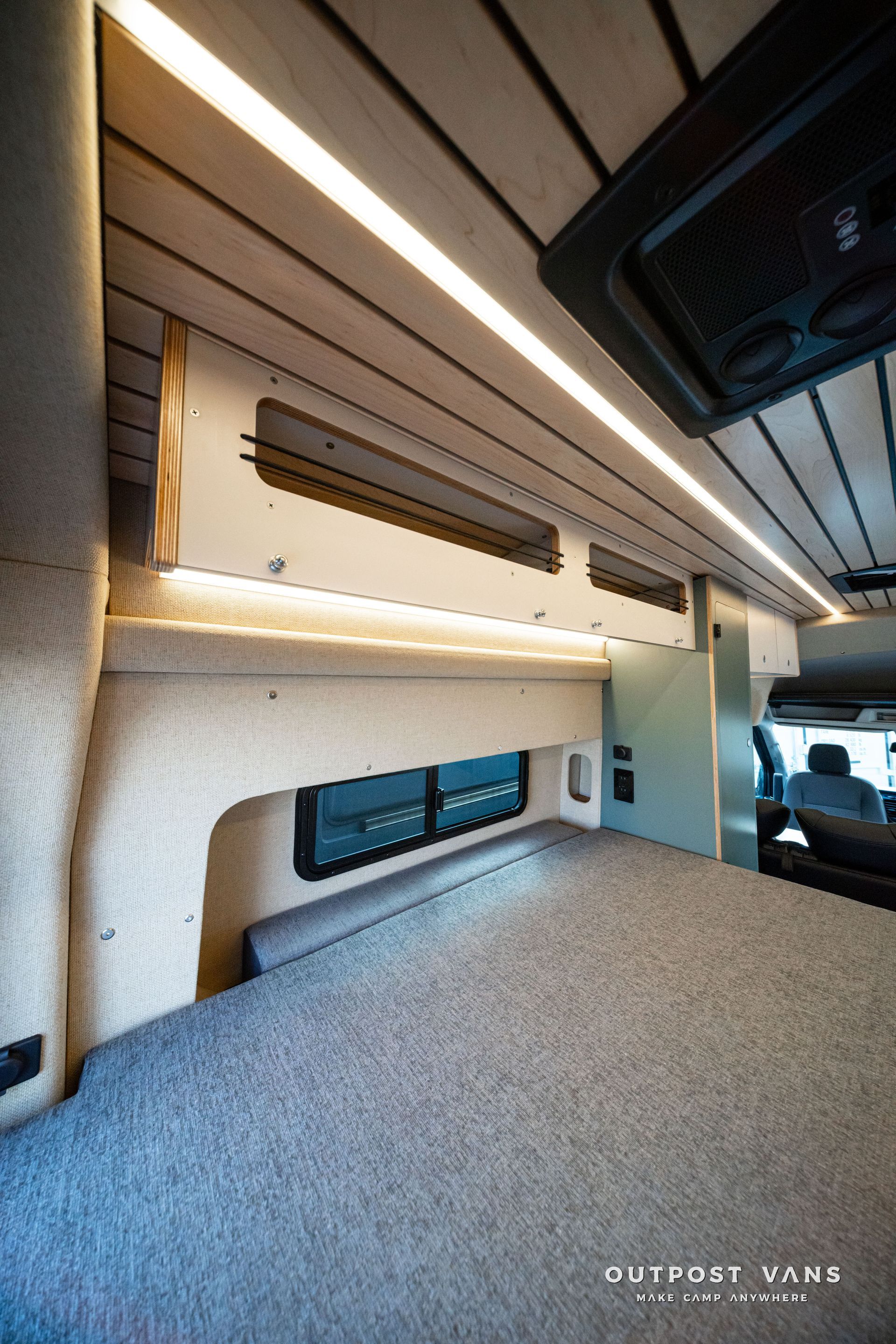 Close-up of a van interior with wood ceiling slats, LED lighting, and a bench seat with storage compartments.