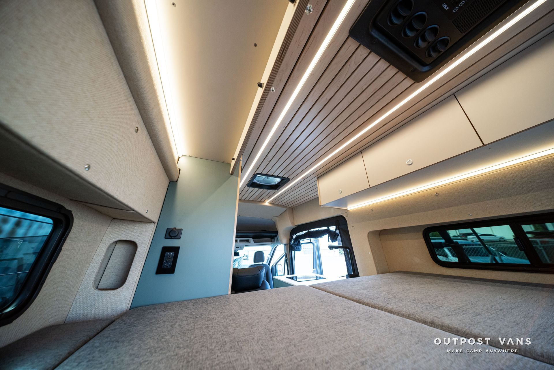 Spacious modern RV interior with beige ceiling lights, wood slats, windows, and a front lounge area.