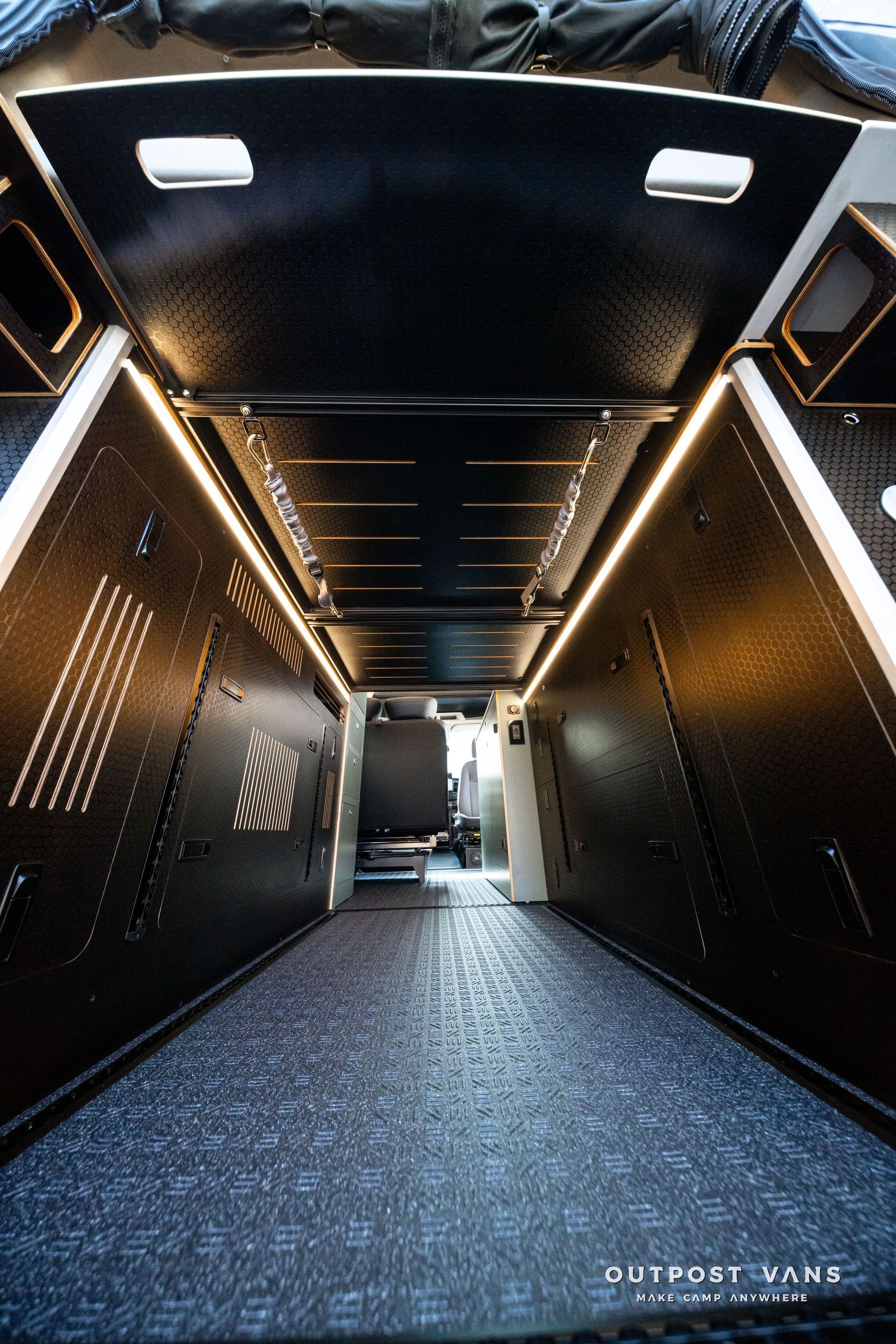 Dark carpeted stairwell with black walls, ceiling lights, and a bright doorway at the bottom