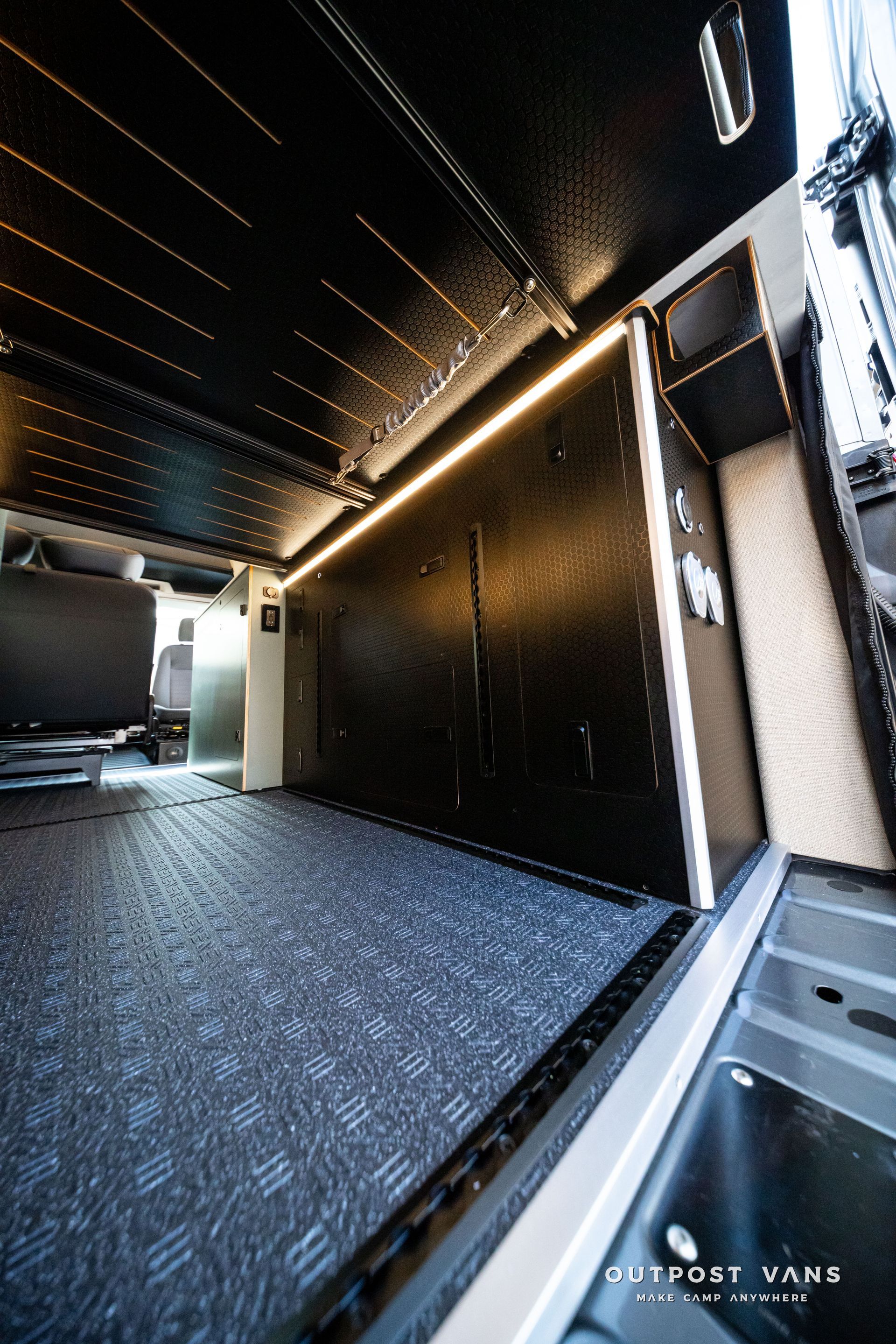 Modern black hallway with patterned carpet, warm LED lighting, and a view into a bright adjacent room