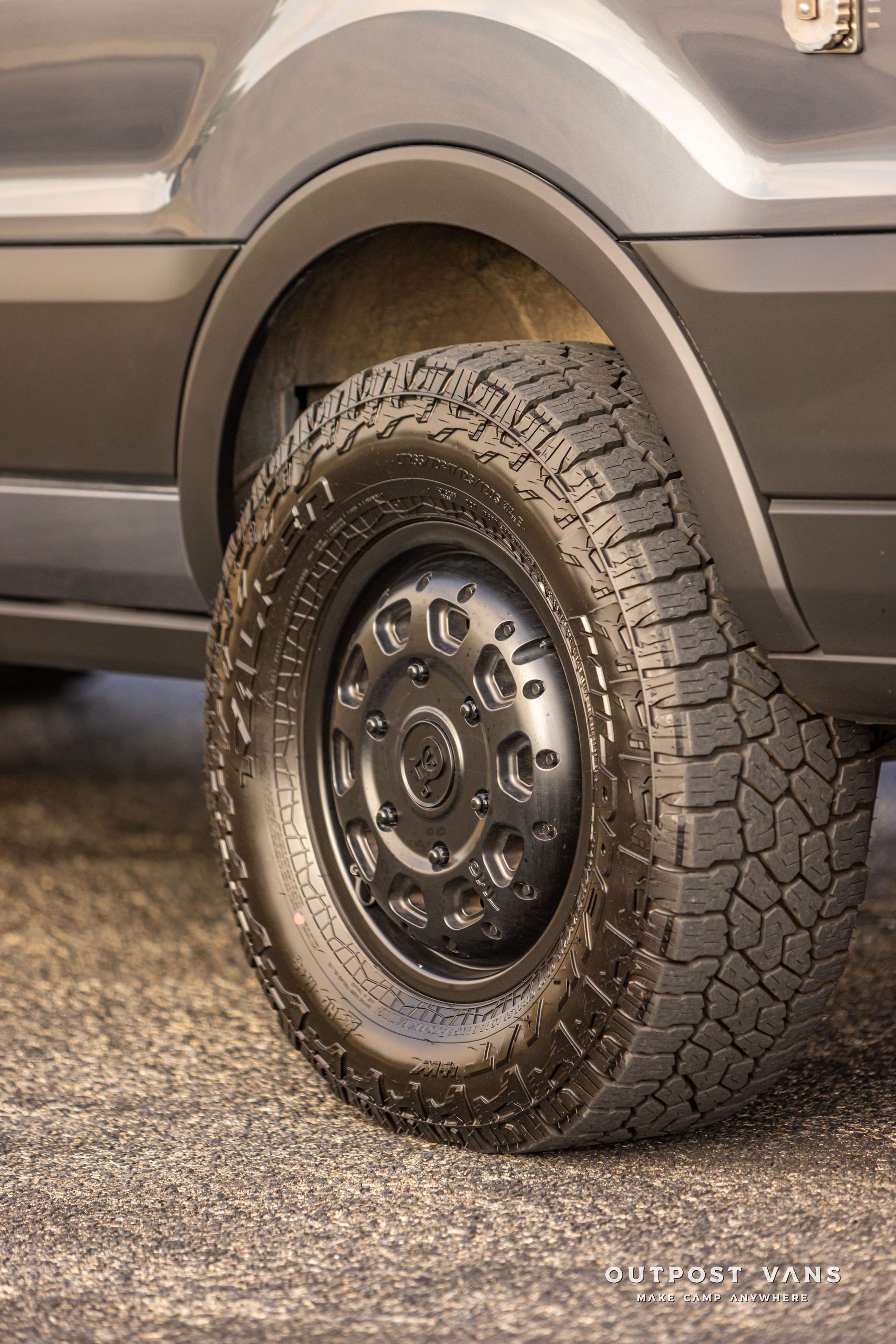 Close-up of a vehicle’s rear wheel with a black steel rim and all-terrain tire on a gray SUV.