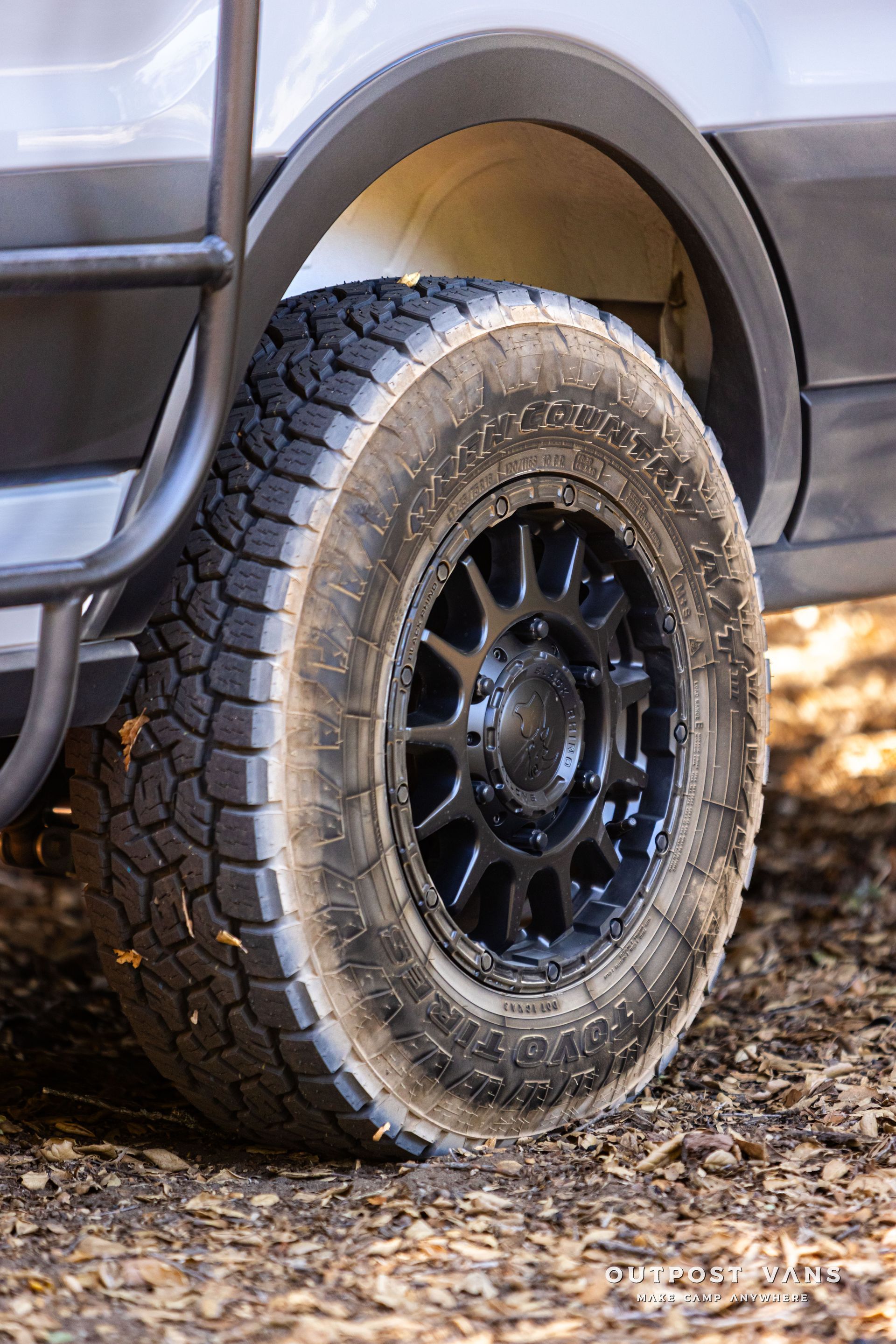 Close-up of an off-road vehicle’s rear tire with black rim on a dirt surface.