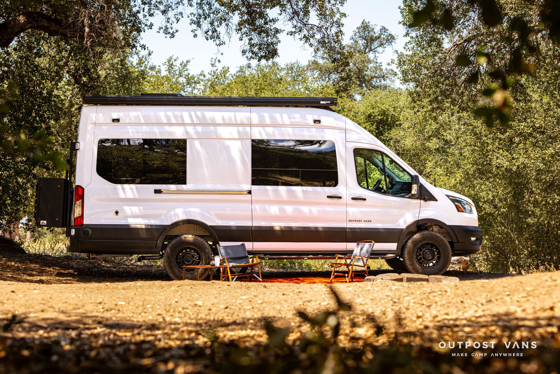 White camper van parked in a wooded area with camping gear underneath.