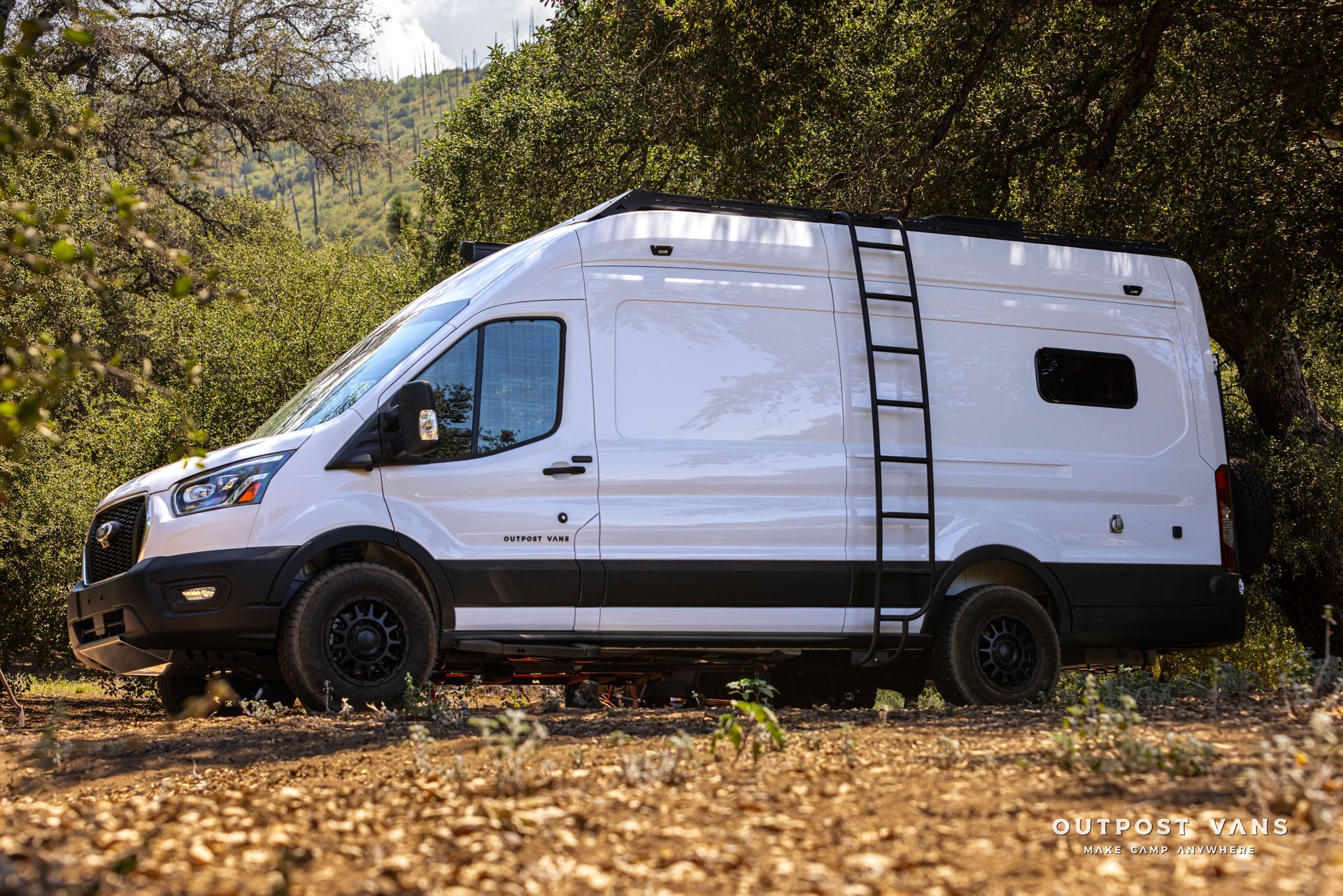 White off-road van parked on a leaf-covered forest path, side view, with roof ladder and black trim