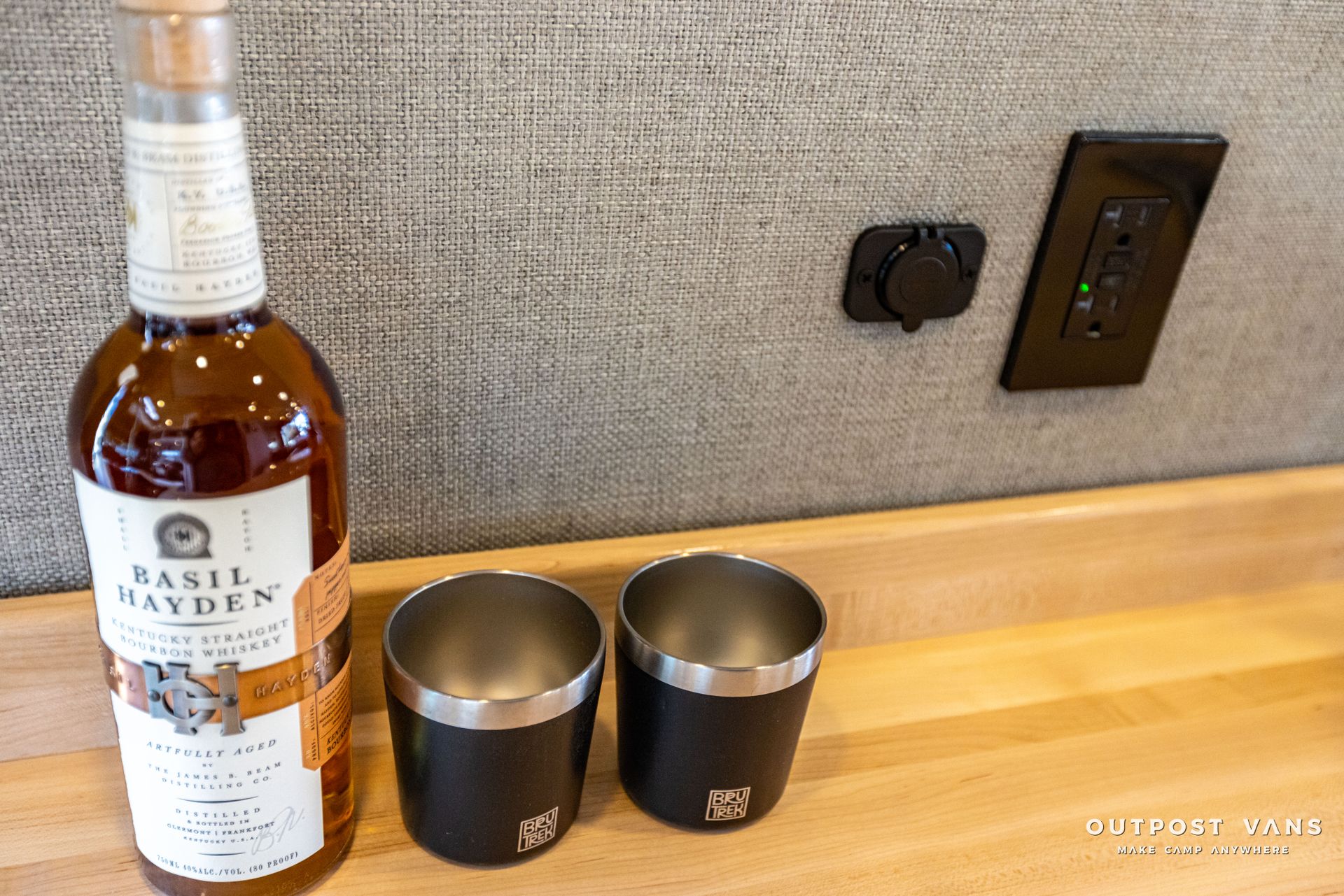 a bottle of whiskey and two cups are on a wooden counter .