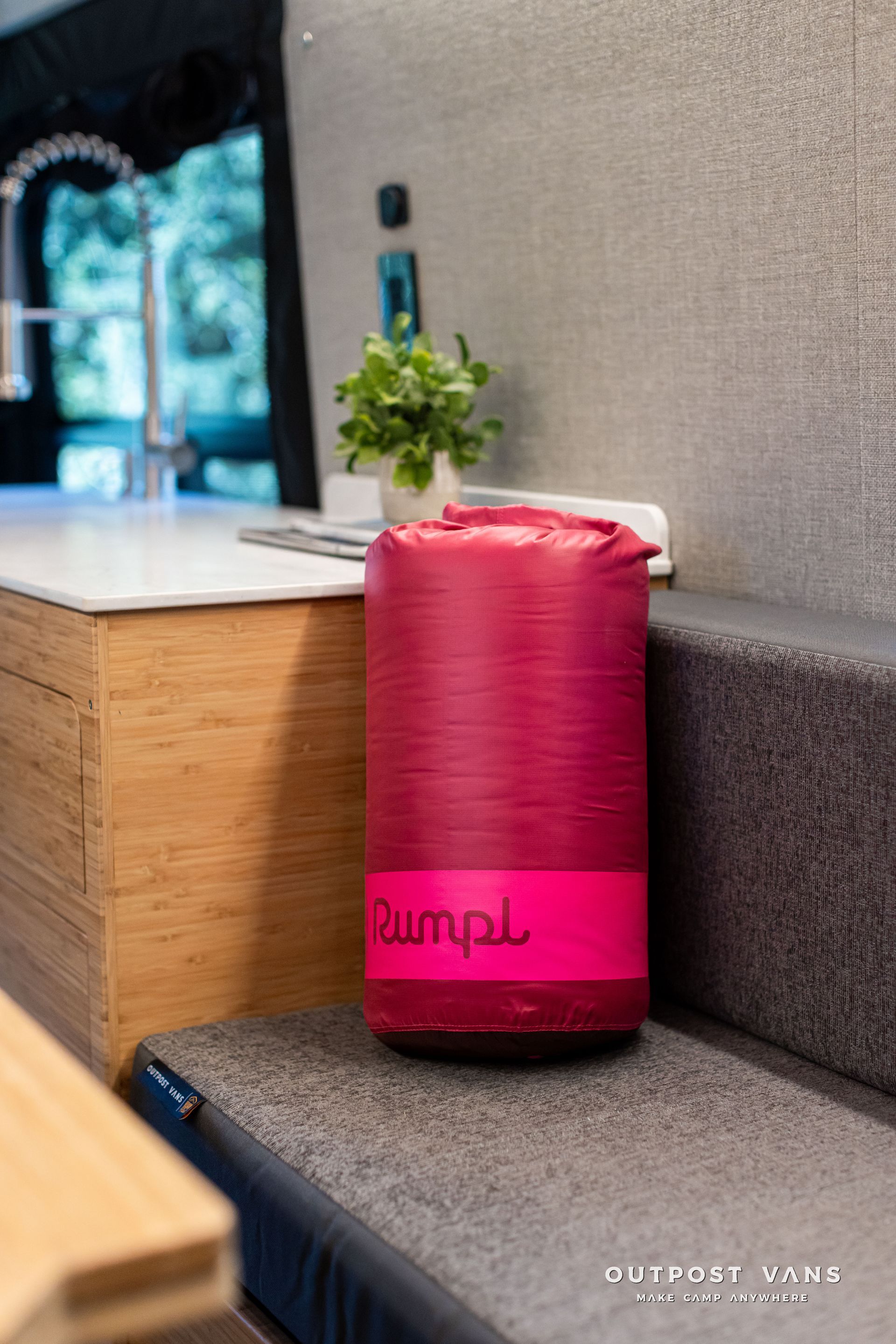 Red cylindrical Bluetooth speaker on a wooden ledge beside a wall and small plant.
