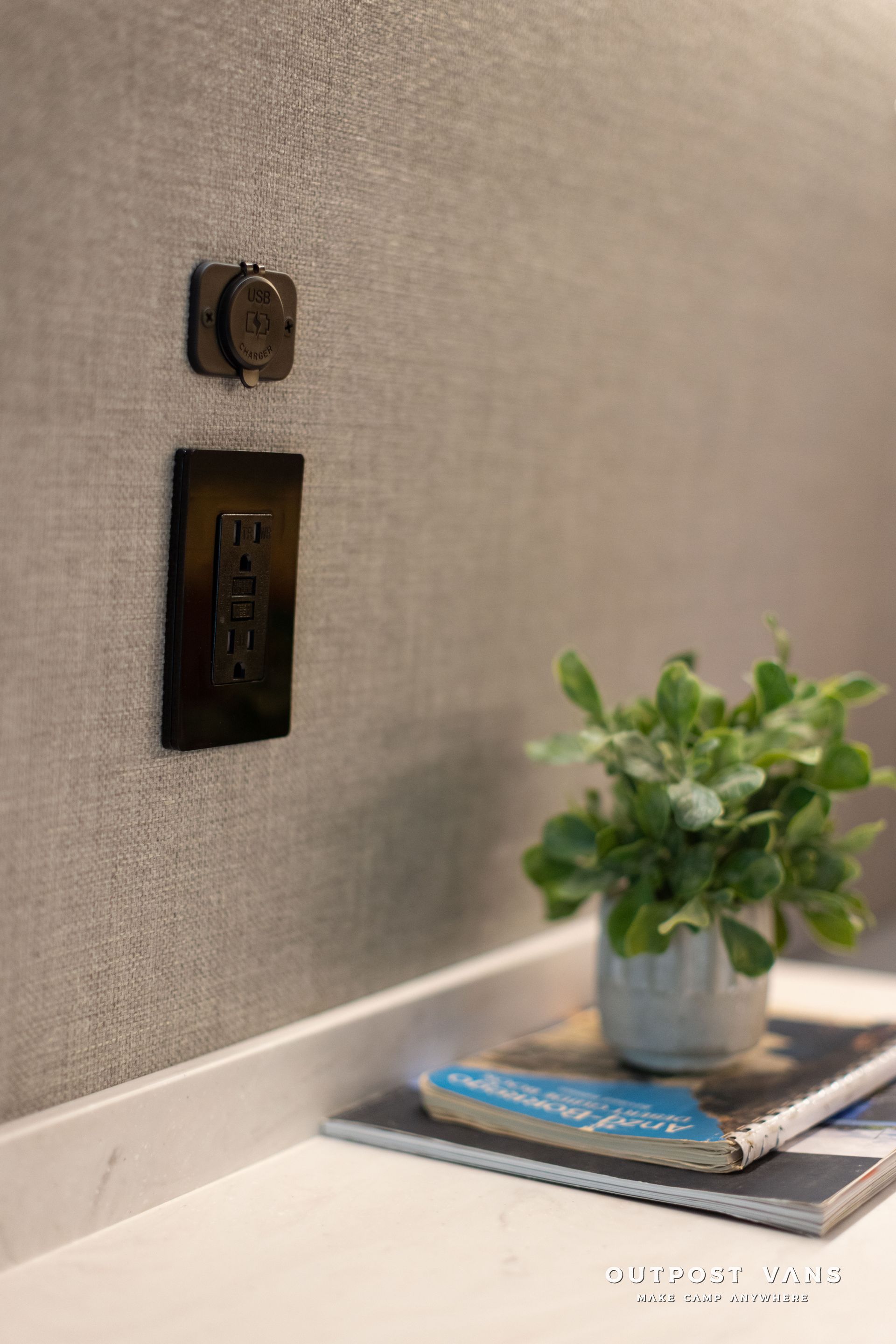Small potted plant on stacked books beside a beige wall with a light switch and outlet