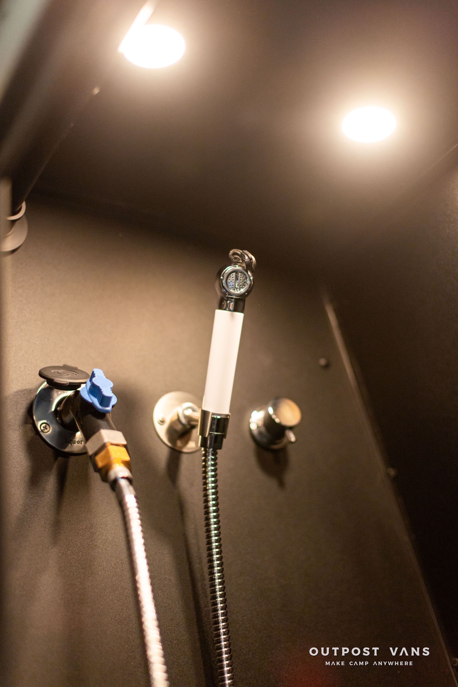 Shower stall with black walls, two recessed lights, and a handheld showerhead with hoses and fixtures.