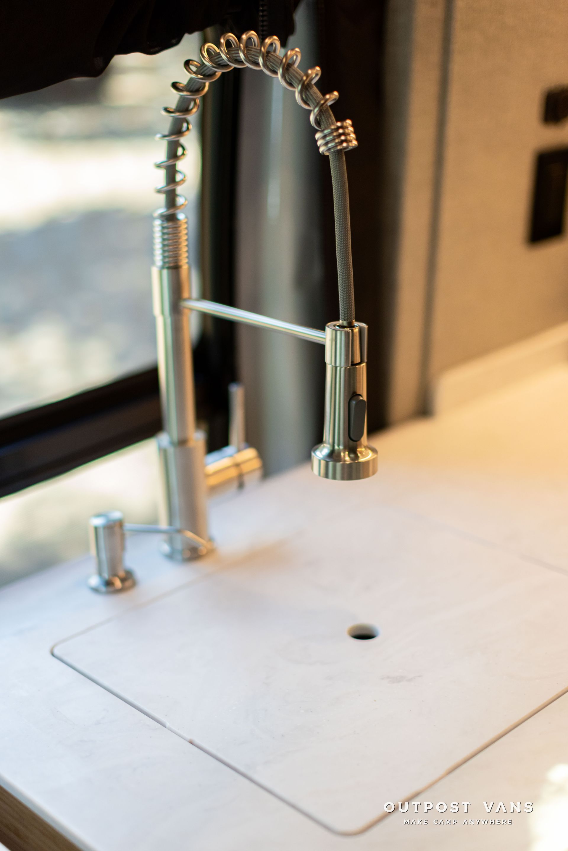Stainless steel kitchen faucet over a white sink with a pull-down sprayer and flexible spring neck