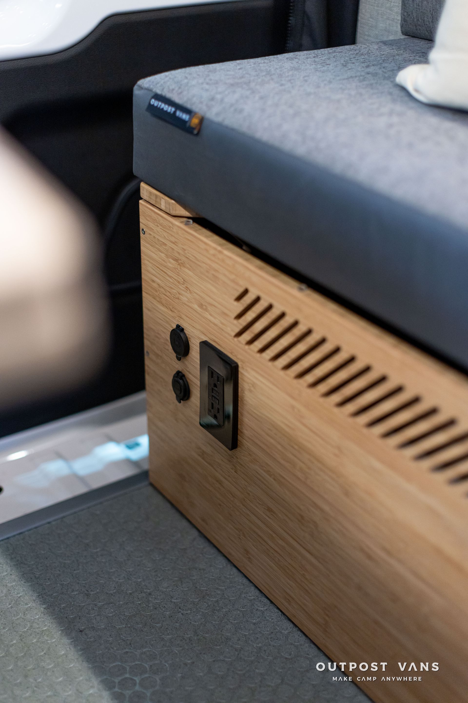 Wood-paneled storage unit with black latch and gray cushion in a vehicle interior