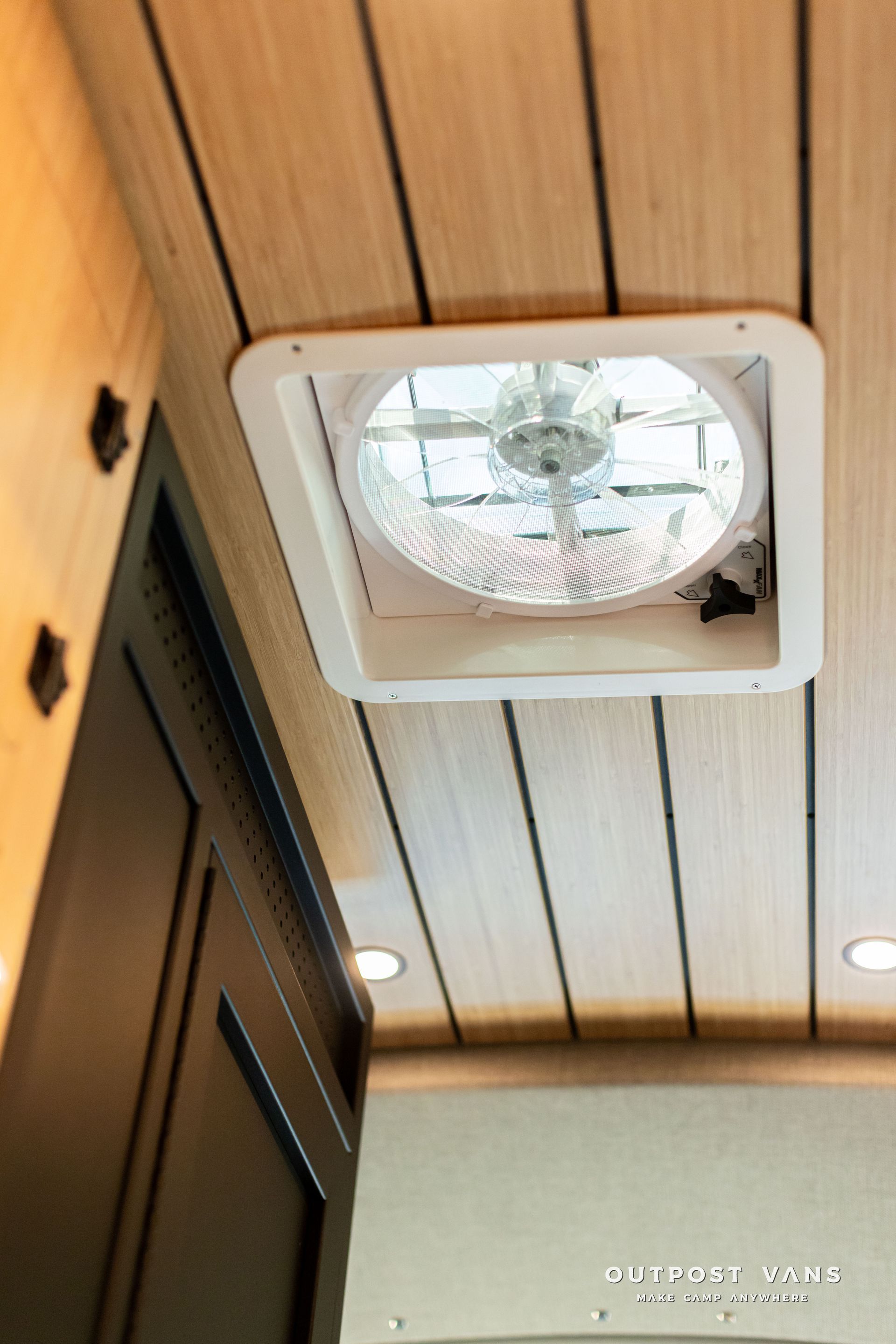 Ceiling vent fan in a wood-paneled interior, with recessed lights and a door frame below.