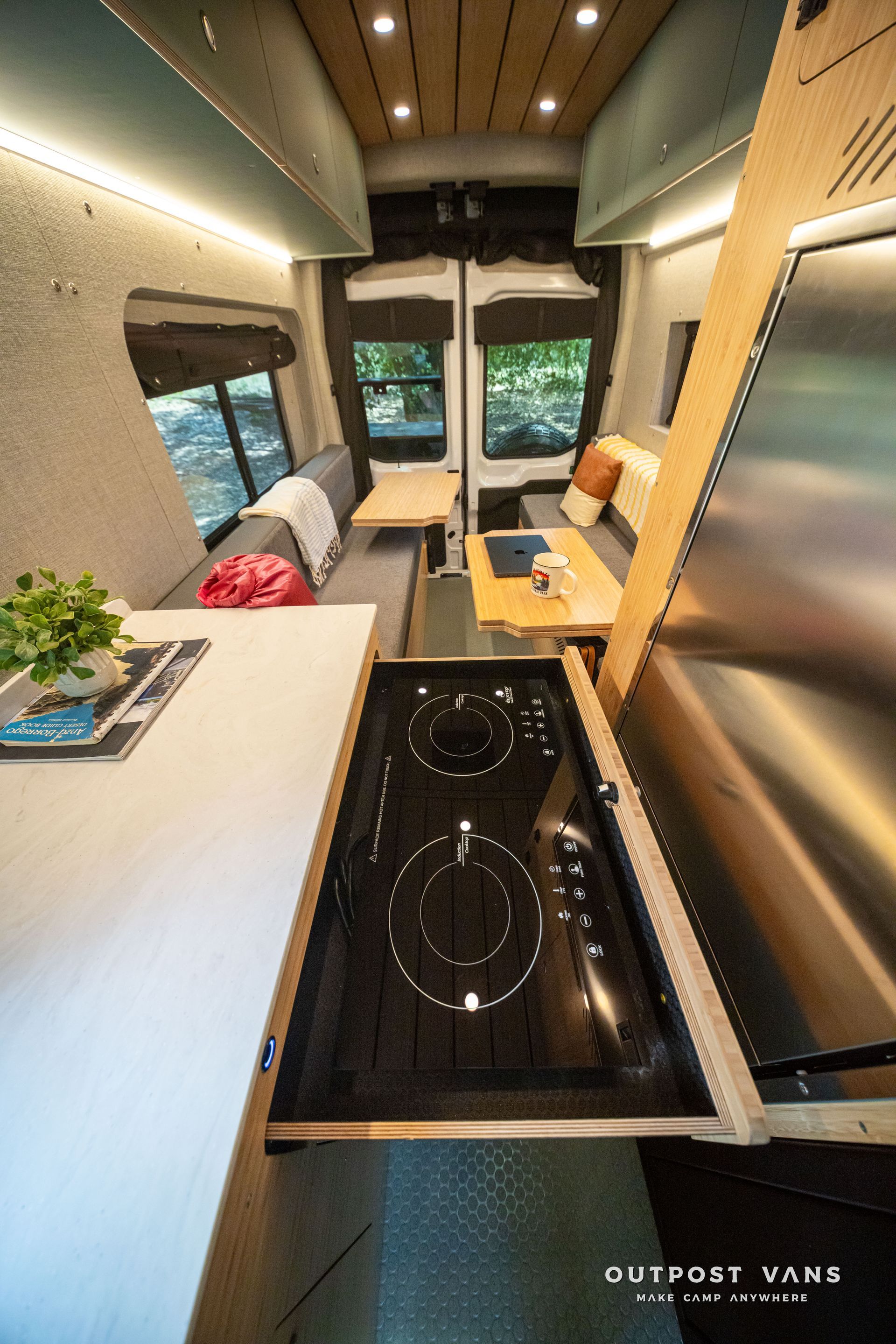 Compact RV kitchen and living area with black stovetop, wood cabinets, and bench seating facing a window.